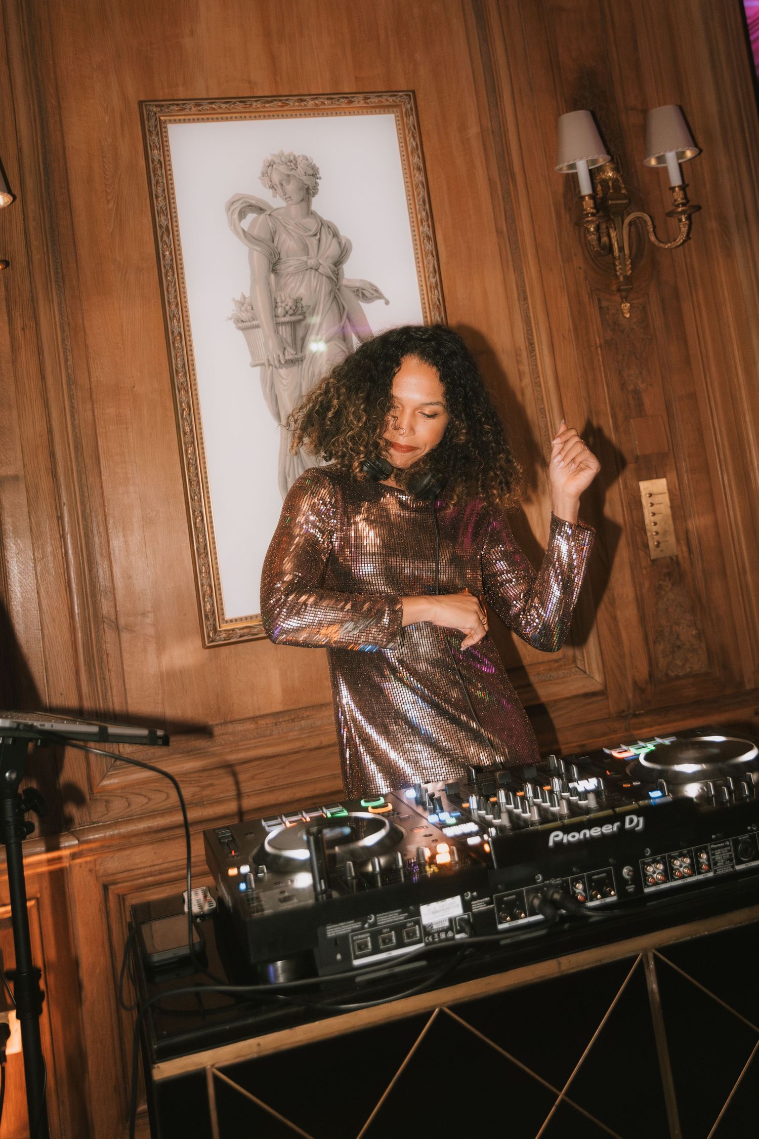 DJ performs on turntables in a wood-paneled room with vintage decor and wall sconces.