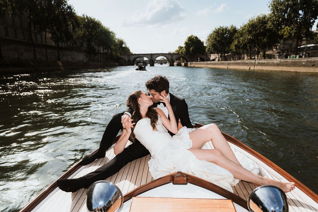 Romantic Paris boat elopement: A couple embracing on a private wooden boat cruise past Seine River monuments without the crowds