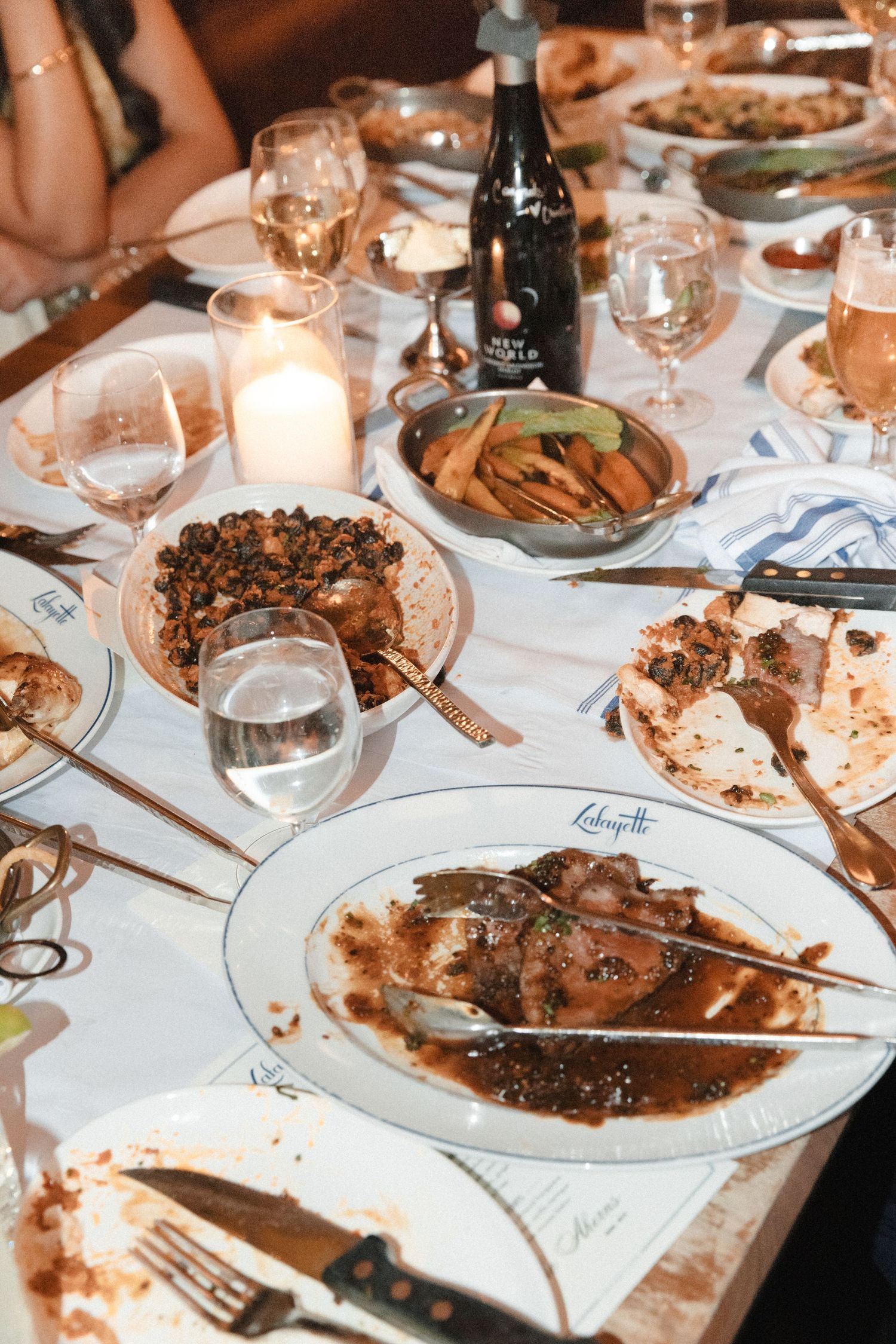 Elegant dinner table at Lafayette restaurant with meat dishes, wine glasses, candles, and shared plates of food.