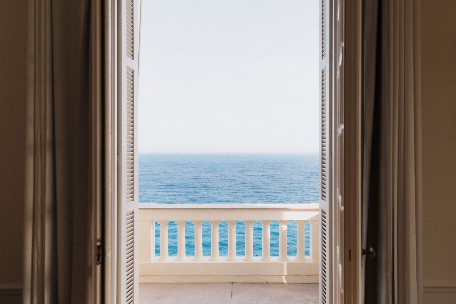 Villa La Vigie, Monaco - Open white French doors leading to a sunlit balcony with elegant railings overlooking a calm blue ocean horizon.