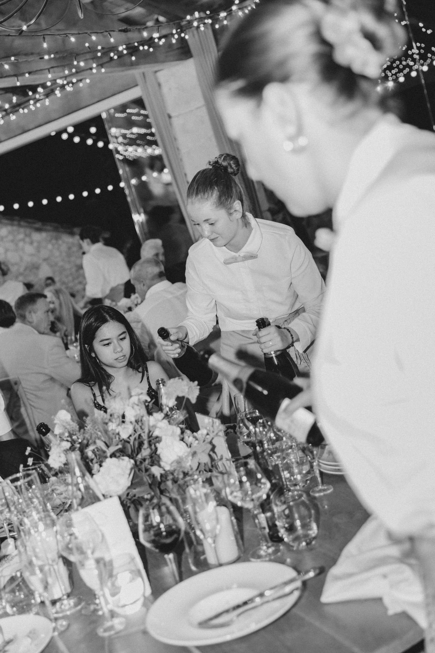 Wedding reception dinner service with string lights overhead and waitstaff serving elegant plated meals.