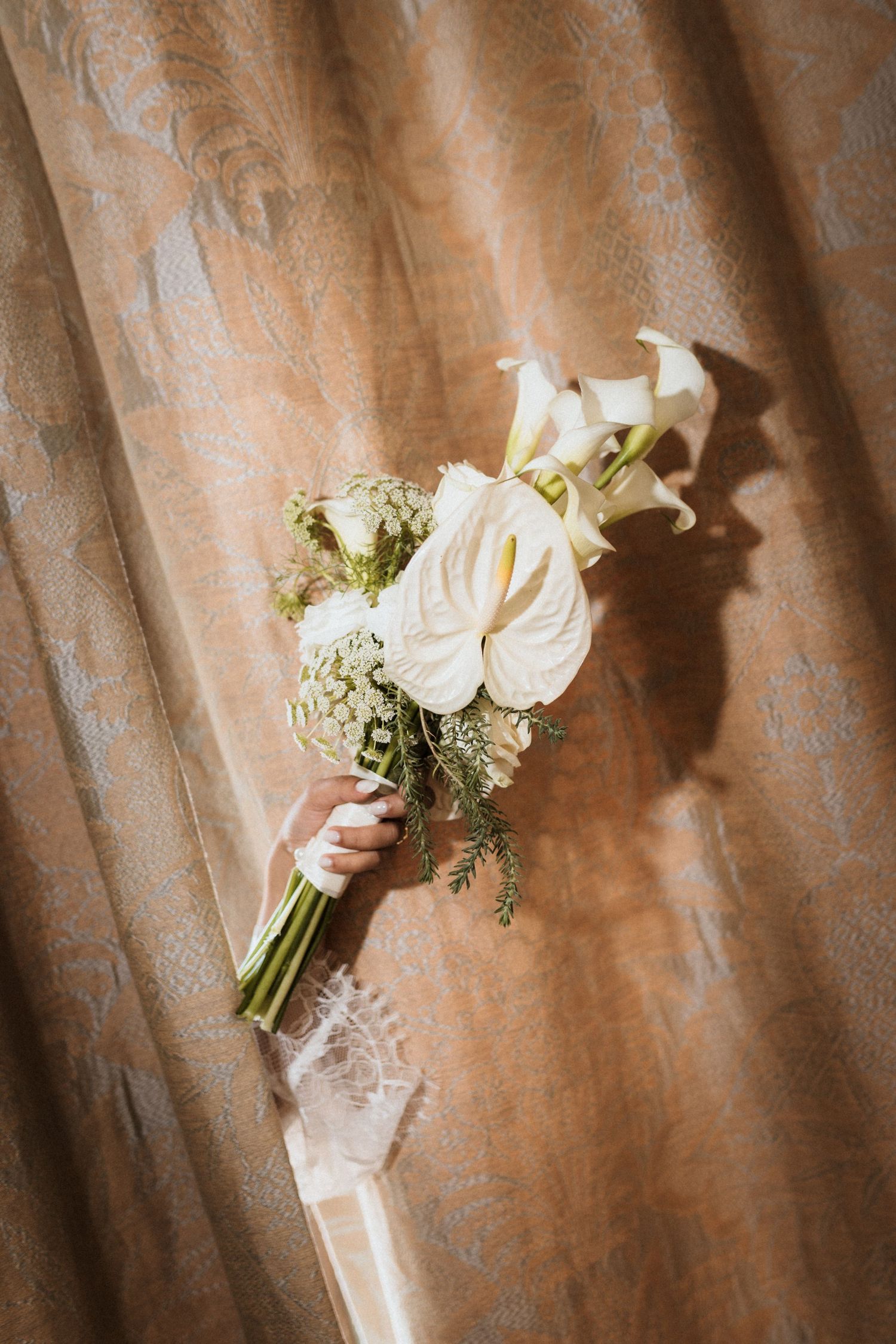 Elegant white rose and greenery wedding bouquet displayed against a textured copper-colored background.