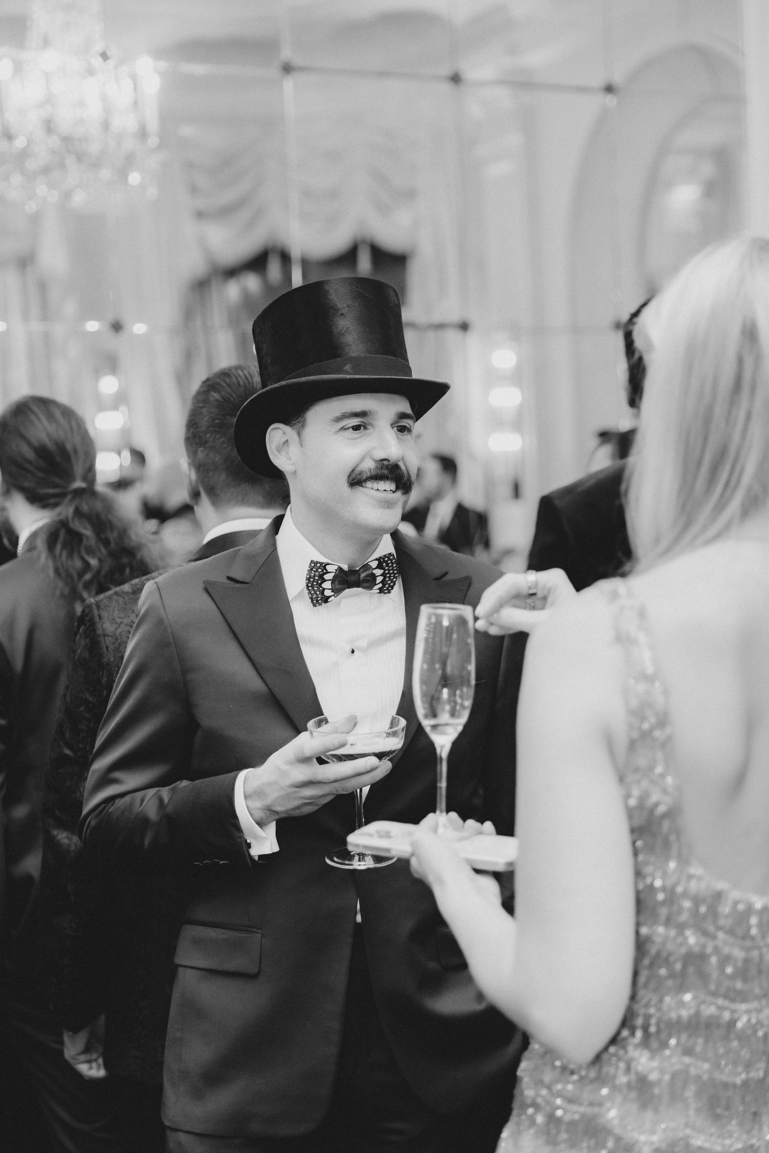 Wedding guests in formal black tie attire enjoy drinks and conversation at an elegant reception.