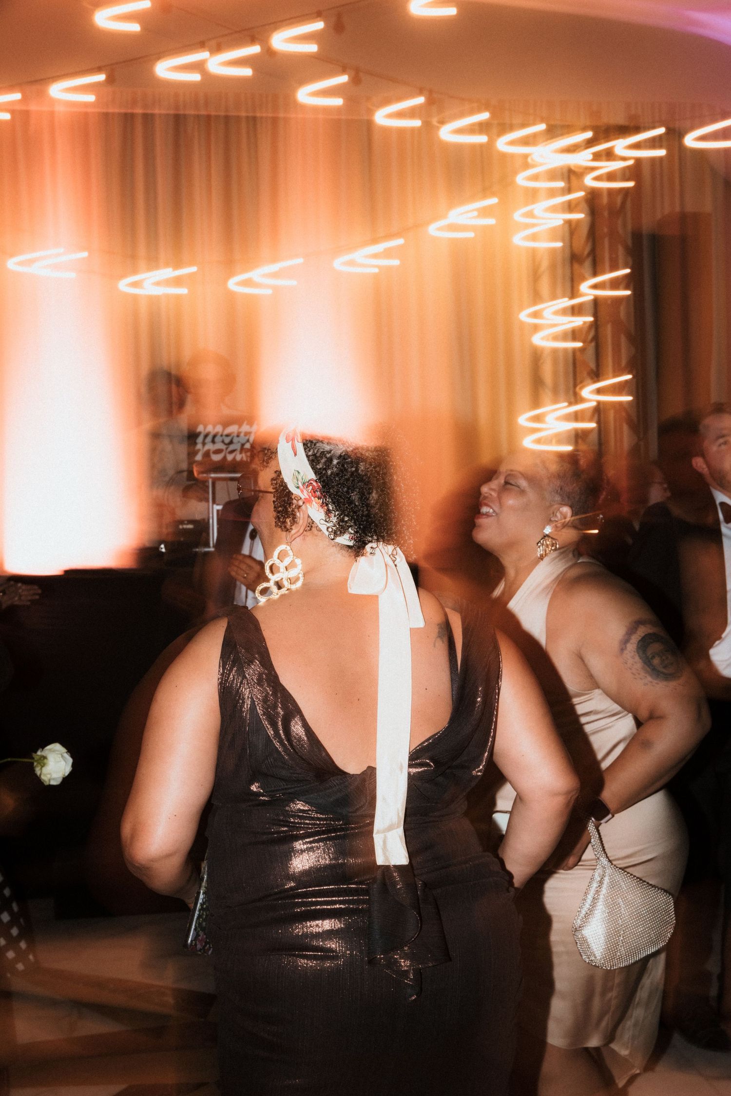 People dancing and having fun at a wedding reception with warm lighting and neon signs on the ceiling.