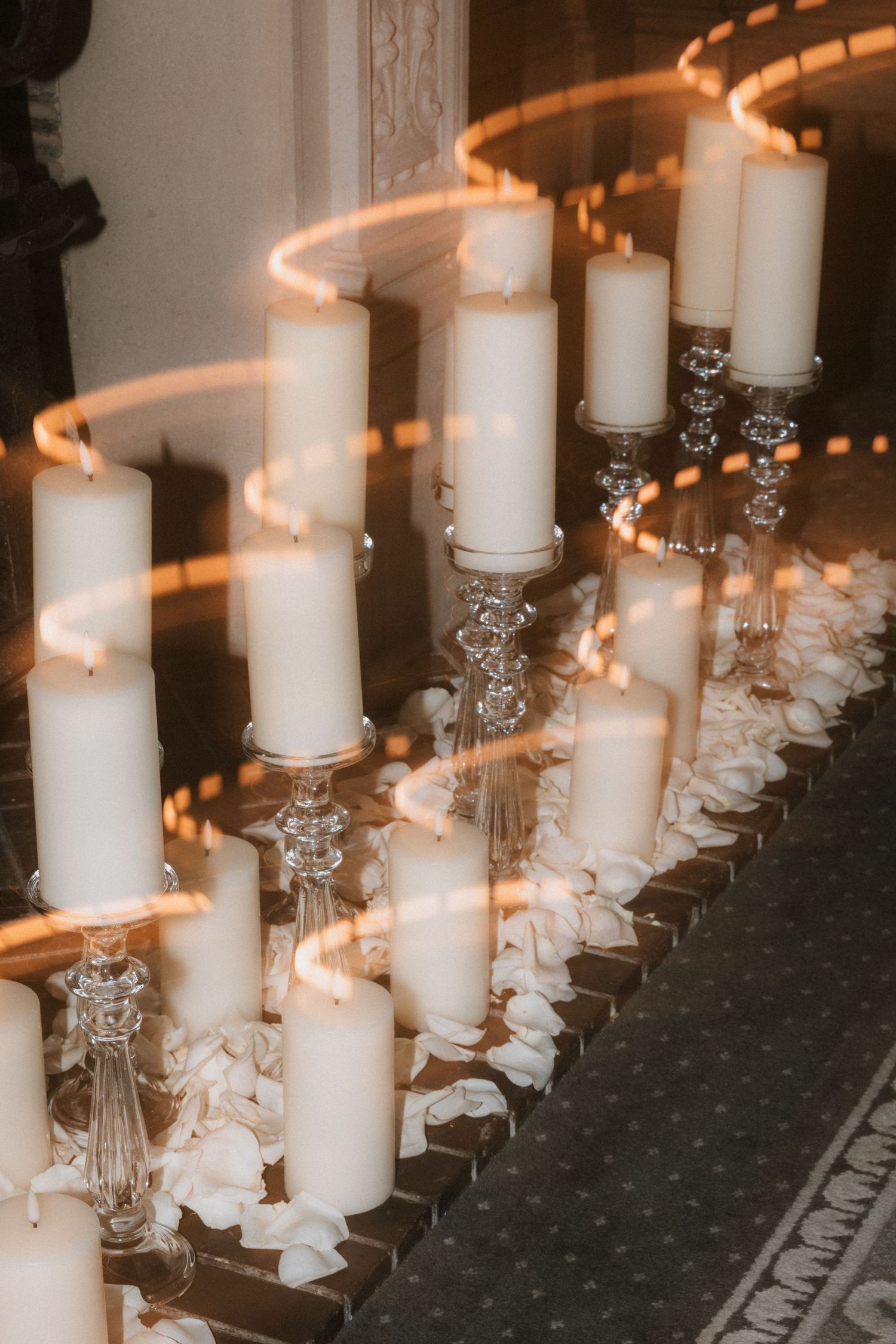 Elegant white pillar candles in crystal holders line up with scattered rose petals creating a romantic wedding aisle decor.