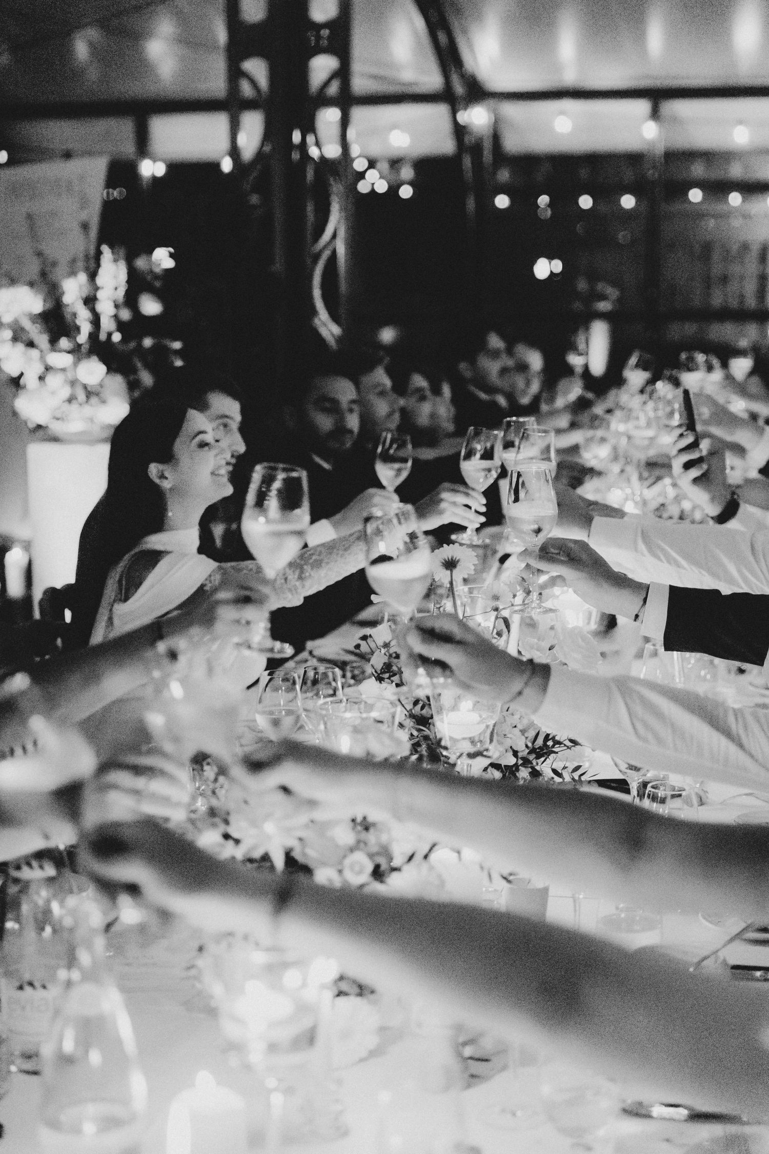 Wedding guests raise glasses in a toast at an elegant candlelit reception dinner table.