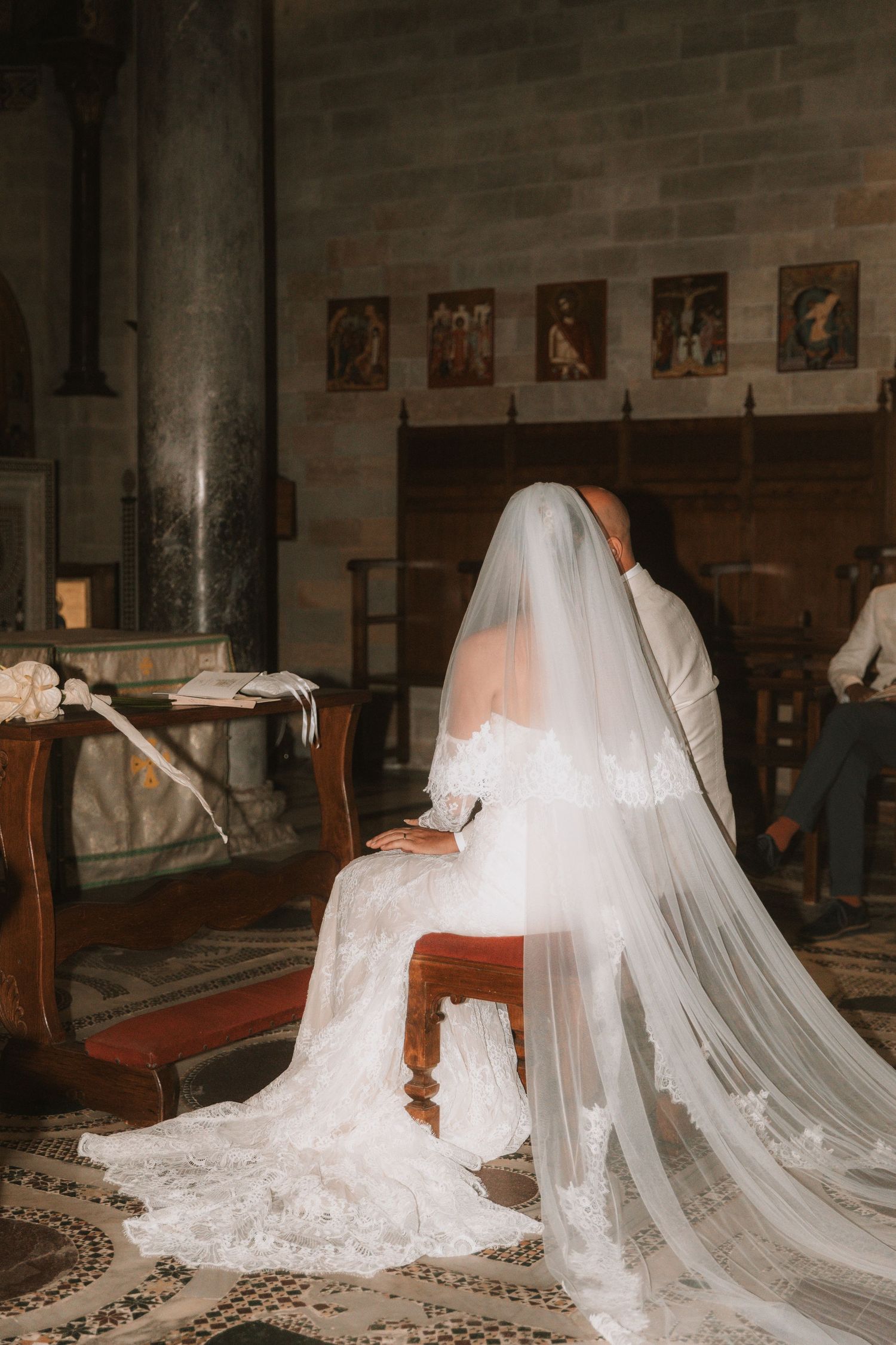 Long flowing white wedding dress veils draped over wooden church pews.