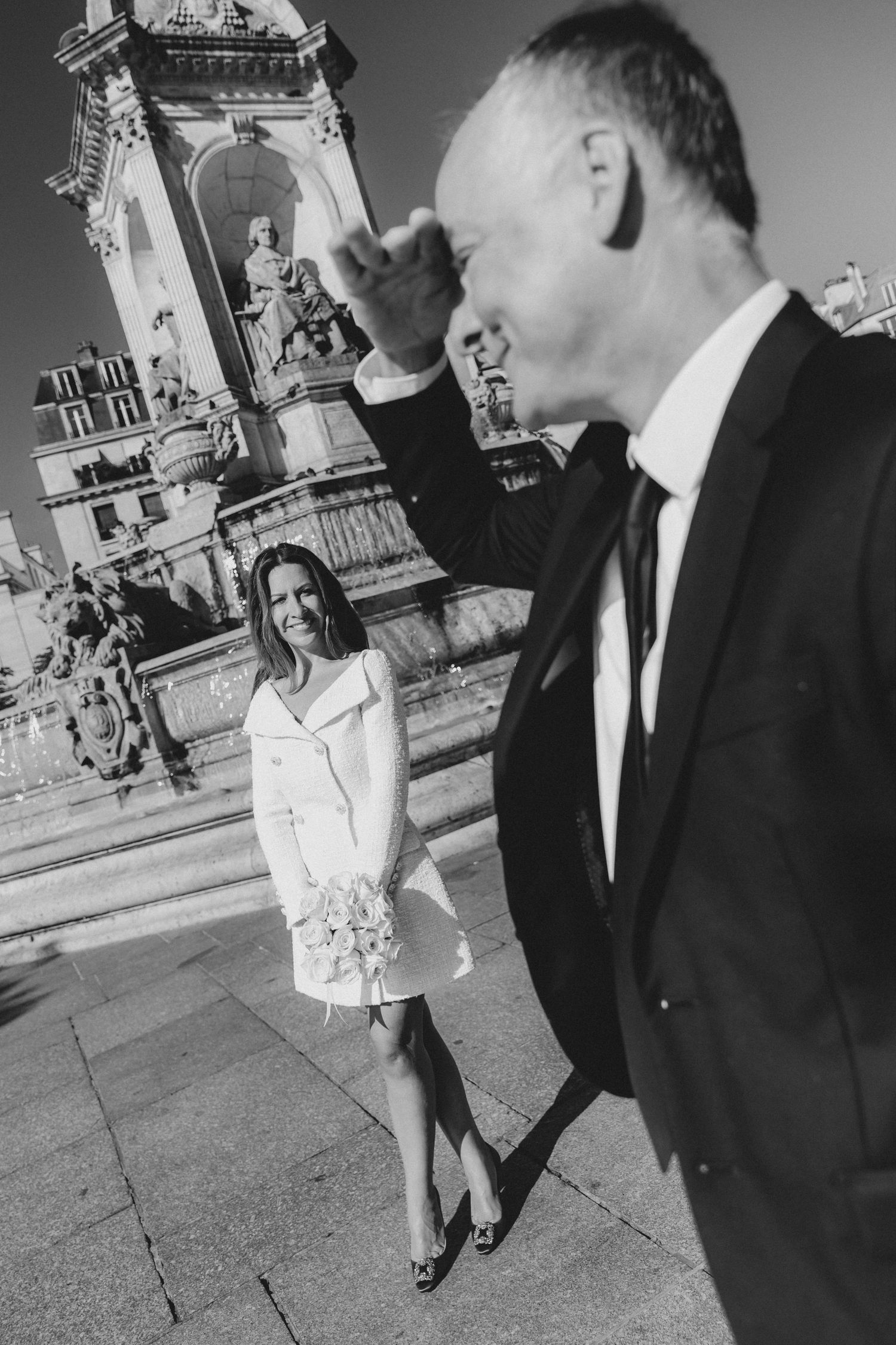 Black and white photo of a couple in formal attire posing at an ornate architectural location.