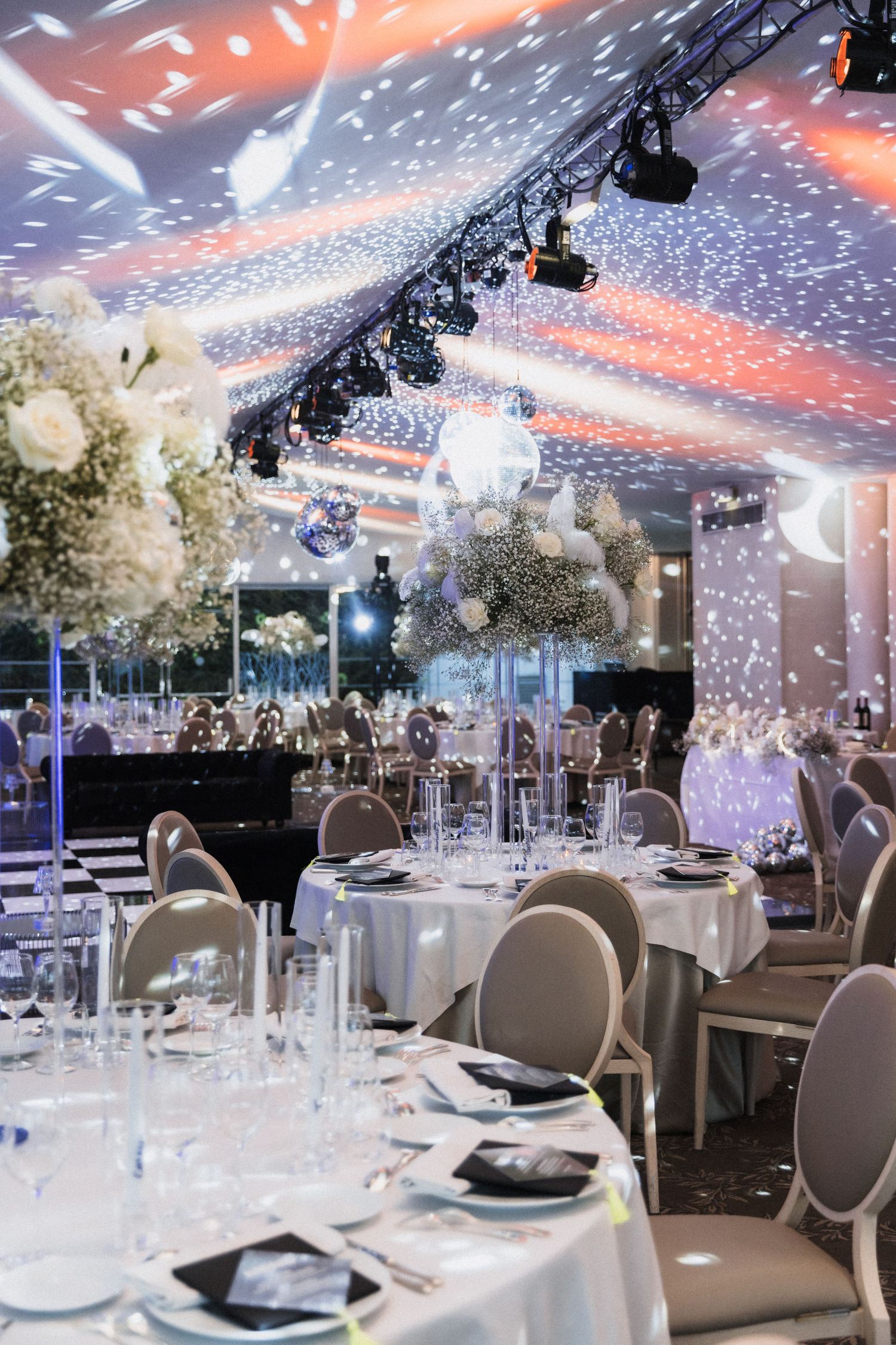 An elegant wedding reception venue with twinkling lights, white floral centerpieces, and modern table settings.