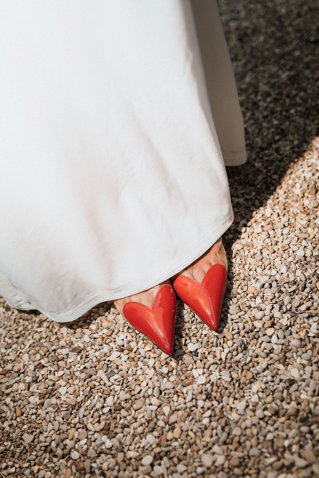 Close-up of red heart-shaped shoes peeking out from under a white wedding dress.