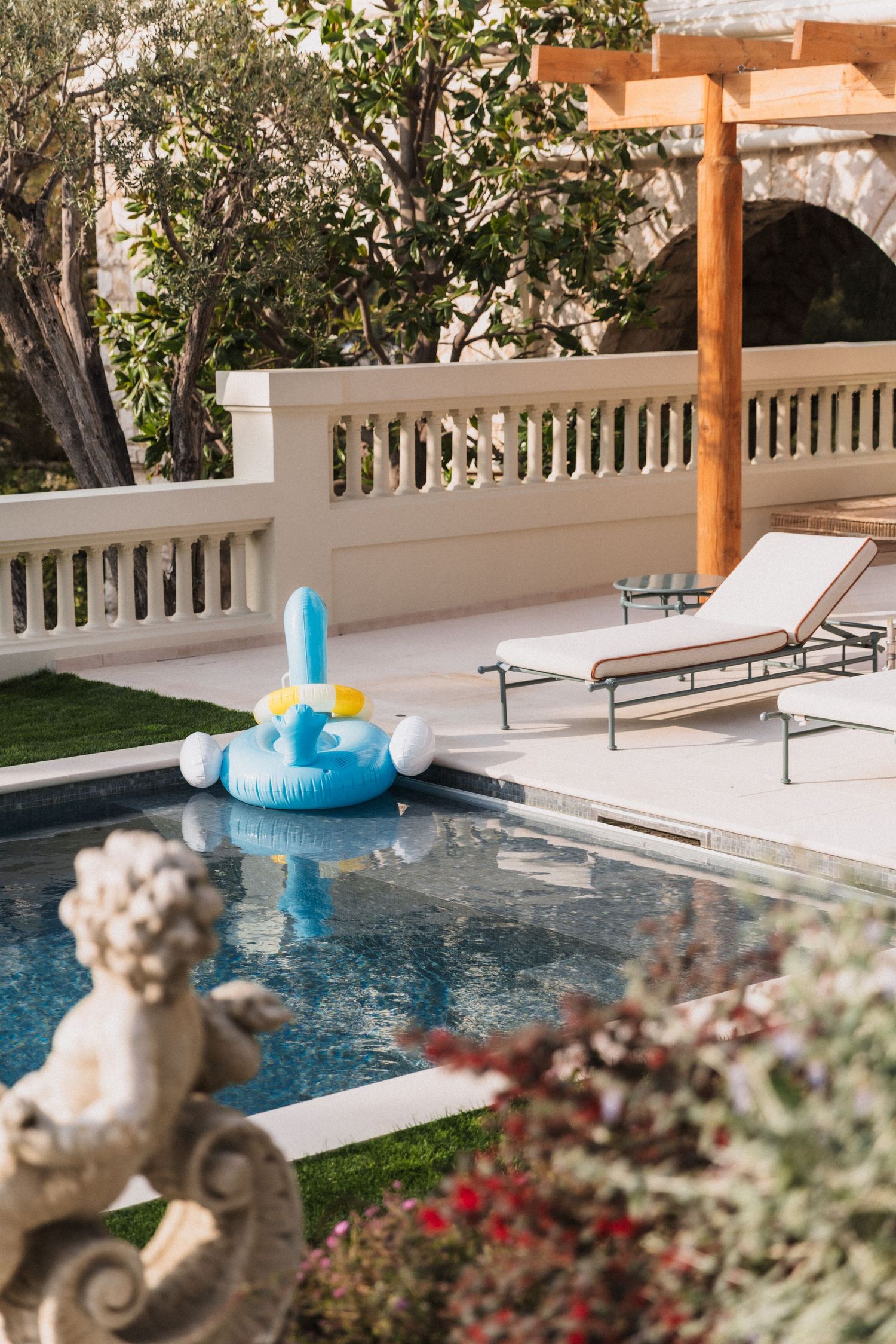 Villa La Vigie, Monaco - Luxury outdoor pool with blue inflatable float, lounge chairs and classical sculpture in lush garden.