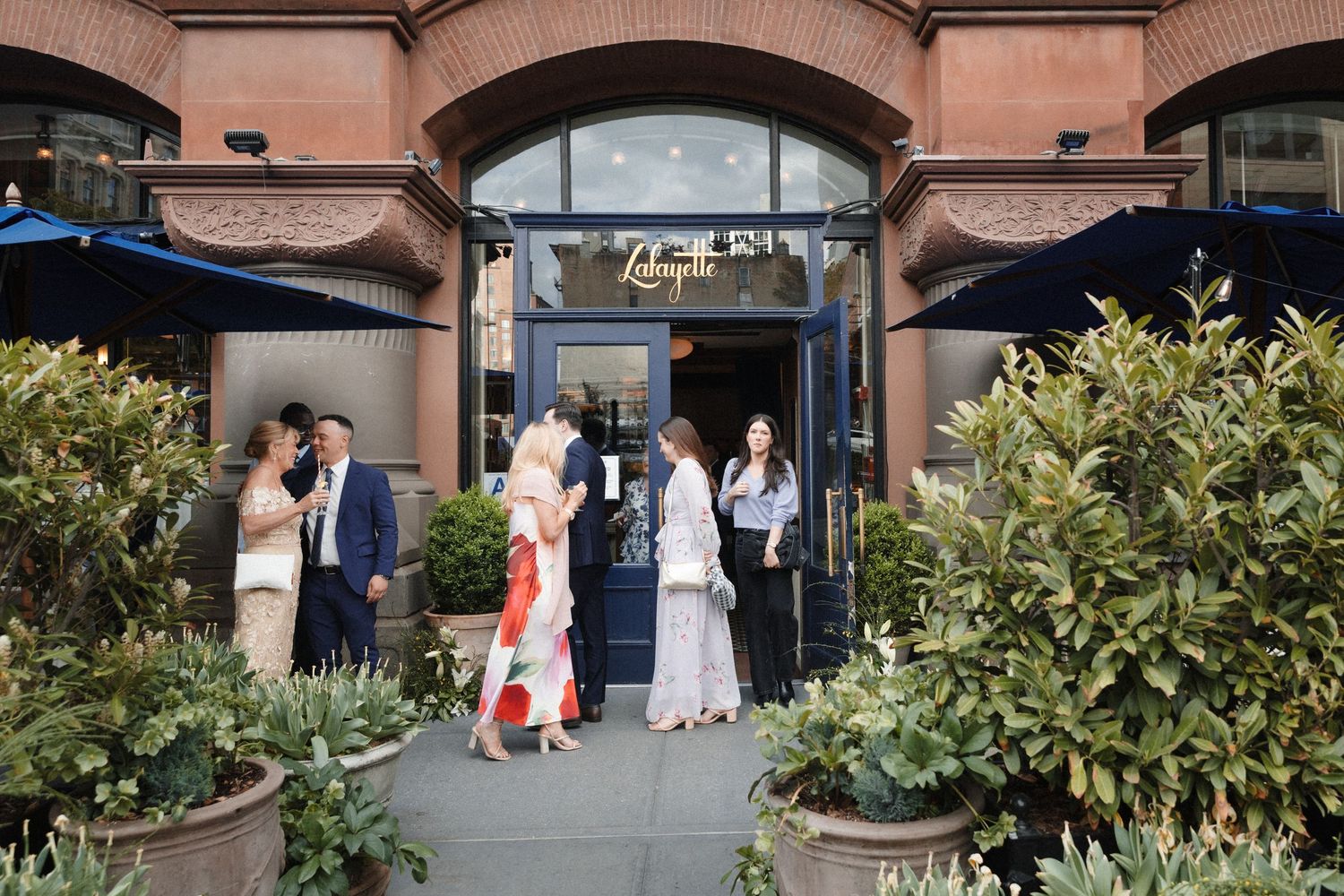 Wedding guests gathering outside Laduree restaurant entrance with blue awnings and brick facade.