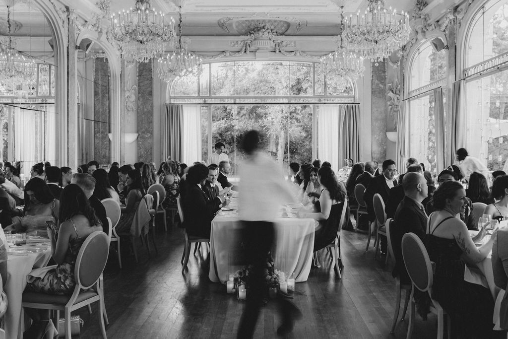 Elegant ballroom wedding reception with crystal chandeliers and guests mingling.
