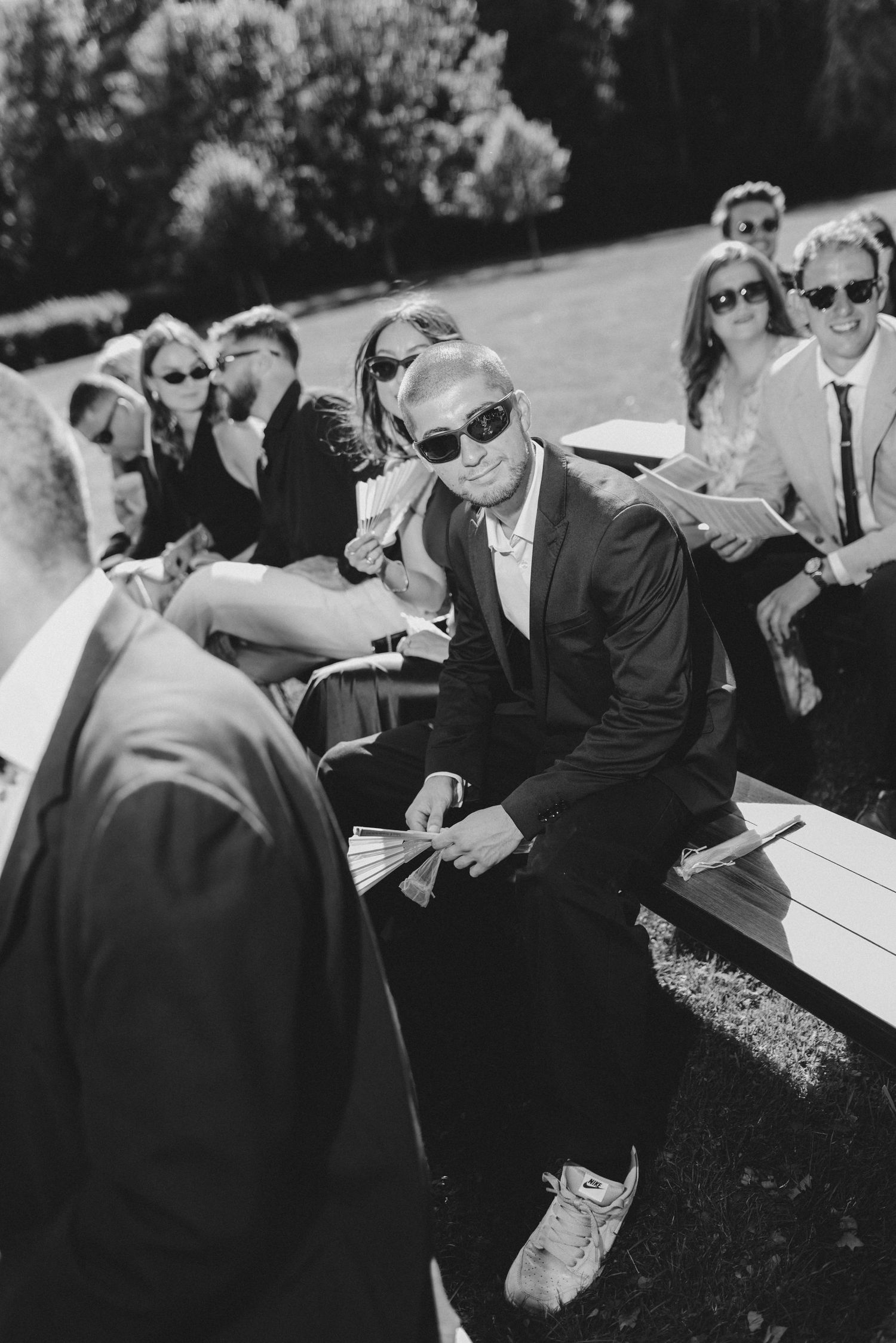 Wedding guests in sunglasses gathered outdoors in black and white photography.