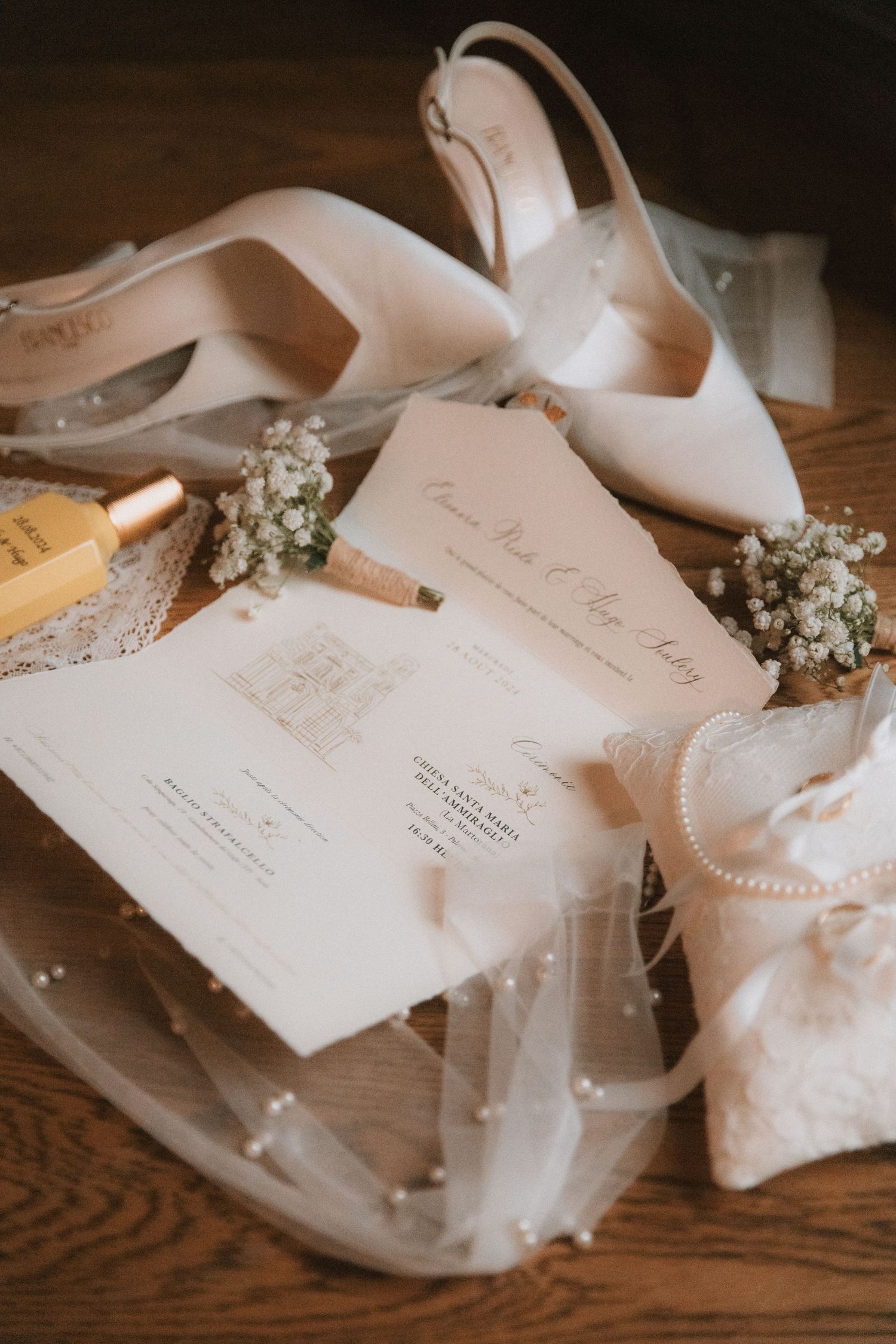 Wedding accessories including white shoes, pearls, and invitation cards arranged on a wooden surface.