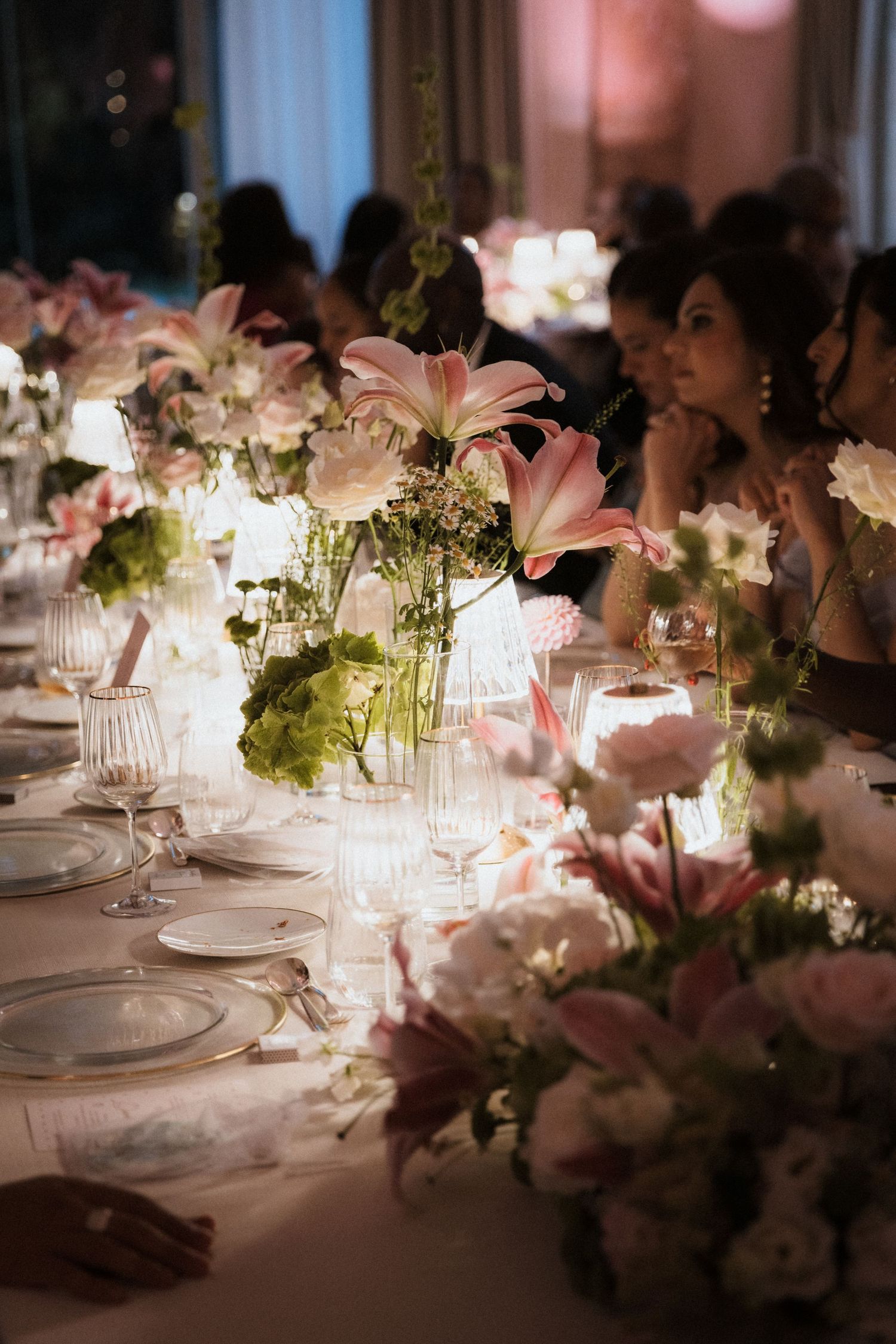 Elegant wedding reception table decorated with pink lilies and glowing candlelight.