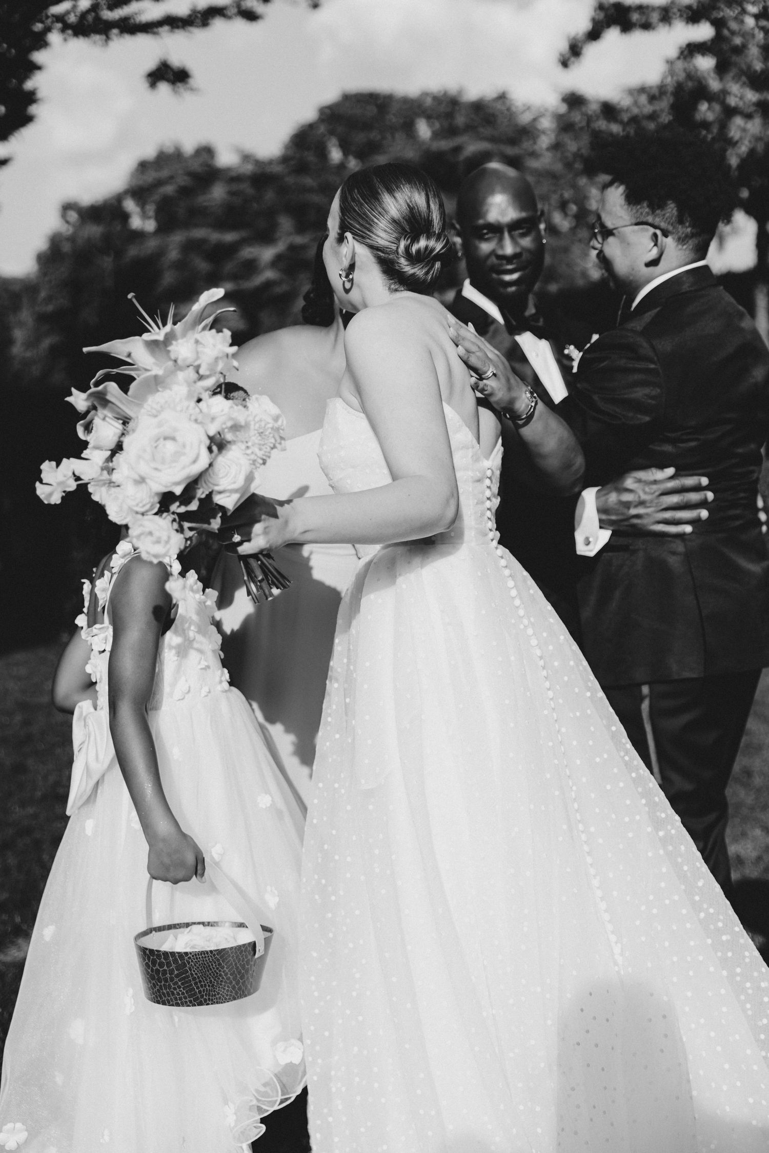 A black and white wedding photo showing people in formal attire during an outdoor ceremony.