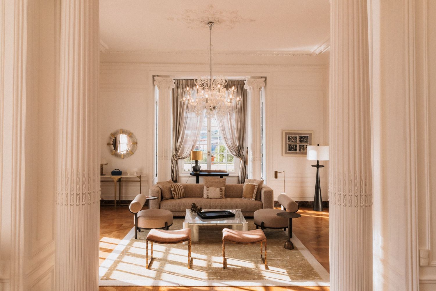 Villa La Vigie, Monaco - Elegant living room with crystal chandelier, curved sofa, white columns, & herringbone floors.