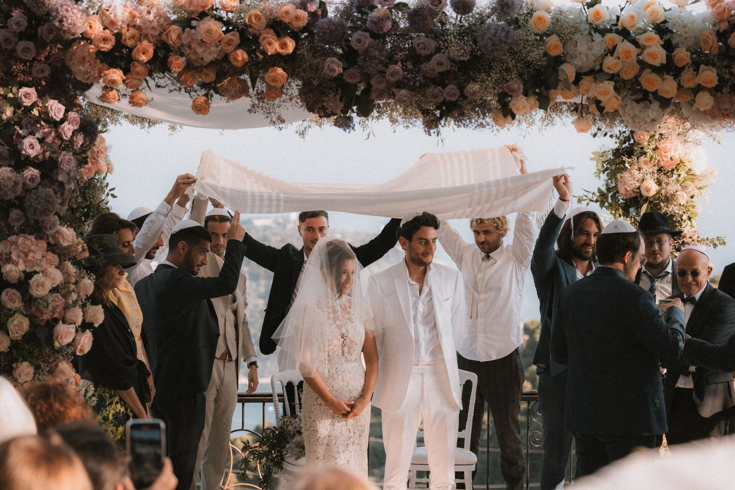 Wedding ceremony setup with floral arch and guests gathered outdoors.
