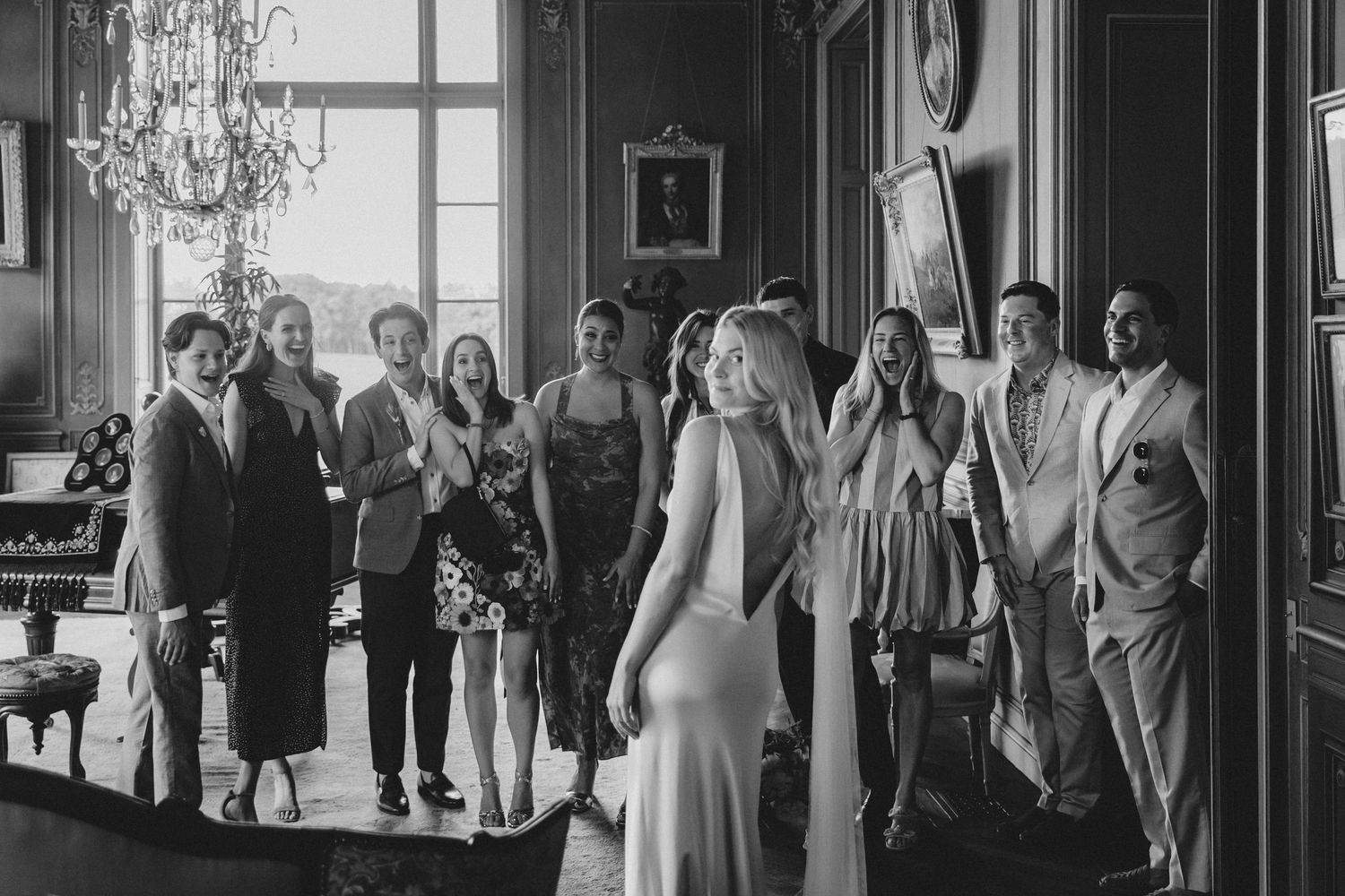 Black and white photo of a bride in a white gown turning to face her wedding guests in an elegant room.