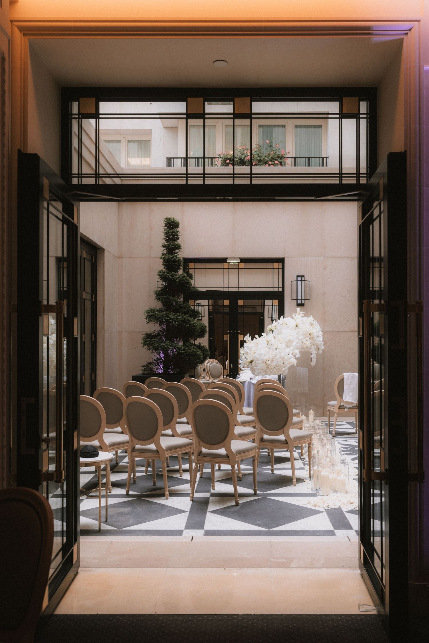 Elegant banquet hall interior with glass walls and upholstered chairs arranged around white-clothed dining tables.