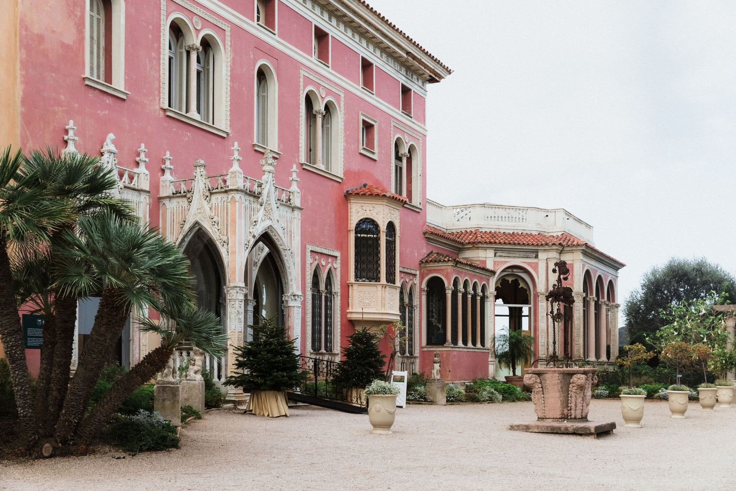 Pink Venetian-style Villa Ephrussi de Rothschild -  with Gothic arches, palm trees, and a colonnaded pavilion in a sunlit courtyard.