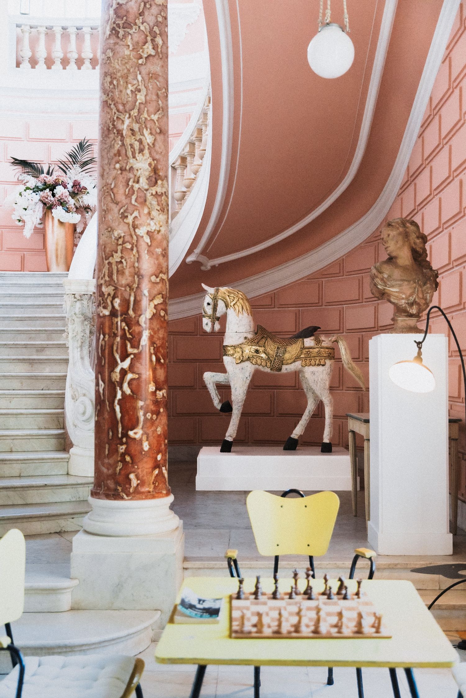 Villa Rocabella - Grand interior with marble columns, carousel horse statue, chess set, and pink ornate staircase.