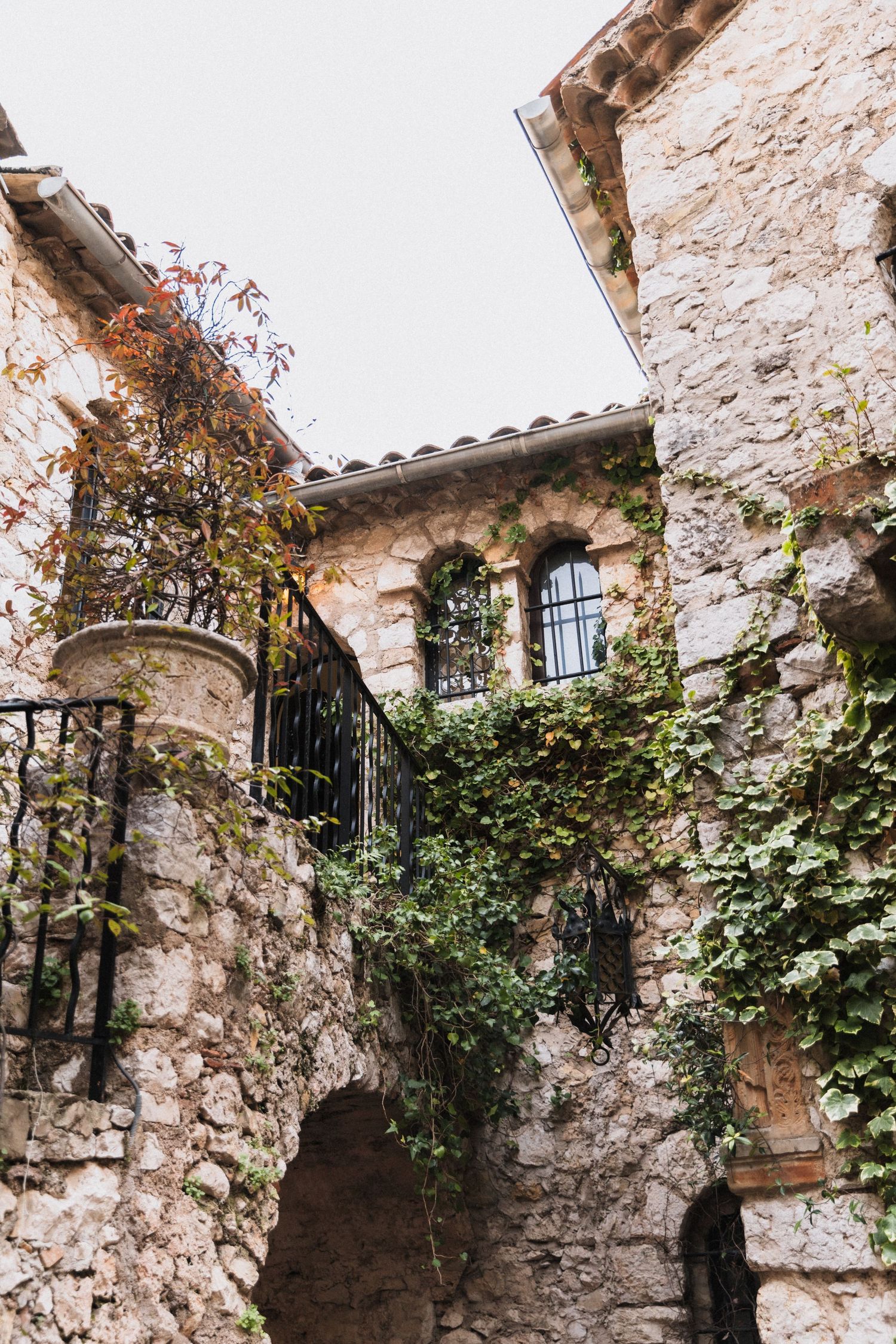 Château Eza - Ancient stone building with ivy-covered walls, arched windows, and wrought iron railings in a medieval village.