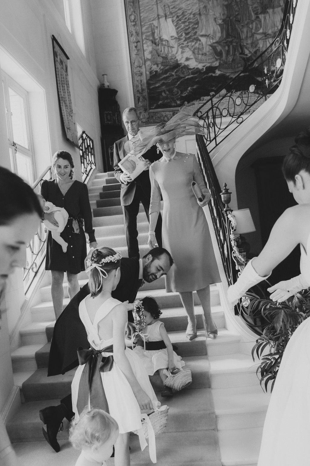 Black and white photograph of people descending an elegant staircase with ornate railings in a vintage setting.