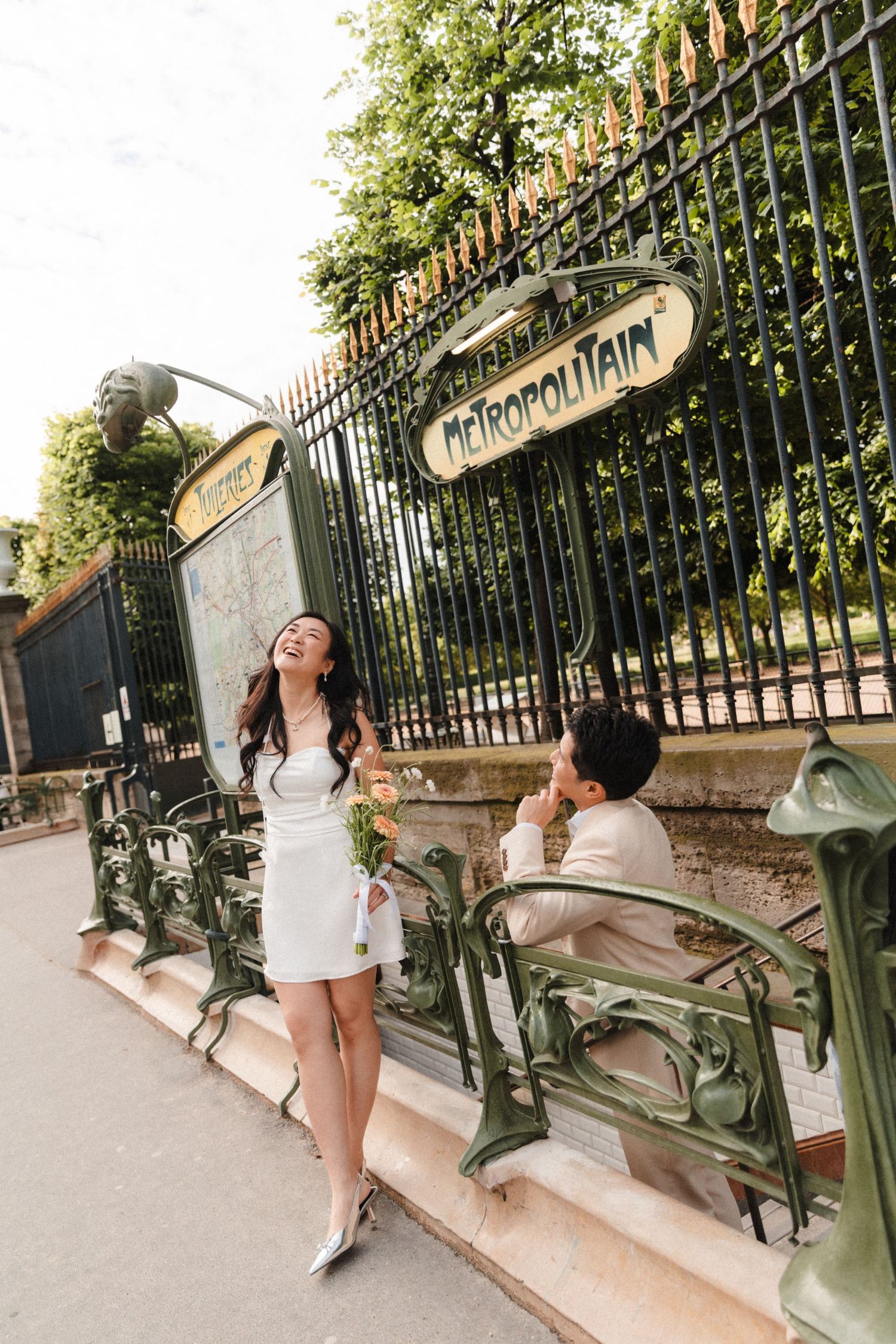 Couple posing at a Paris Metro Metropolitain entrance with Art Nouveau ironwork and lush greenery.