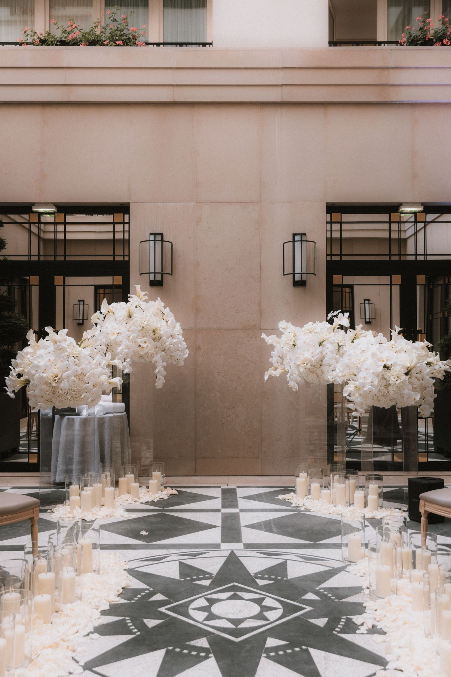 Elegant white floral centerpieces and candles arranged around a geometric floor pattern at a luxury event venue.