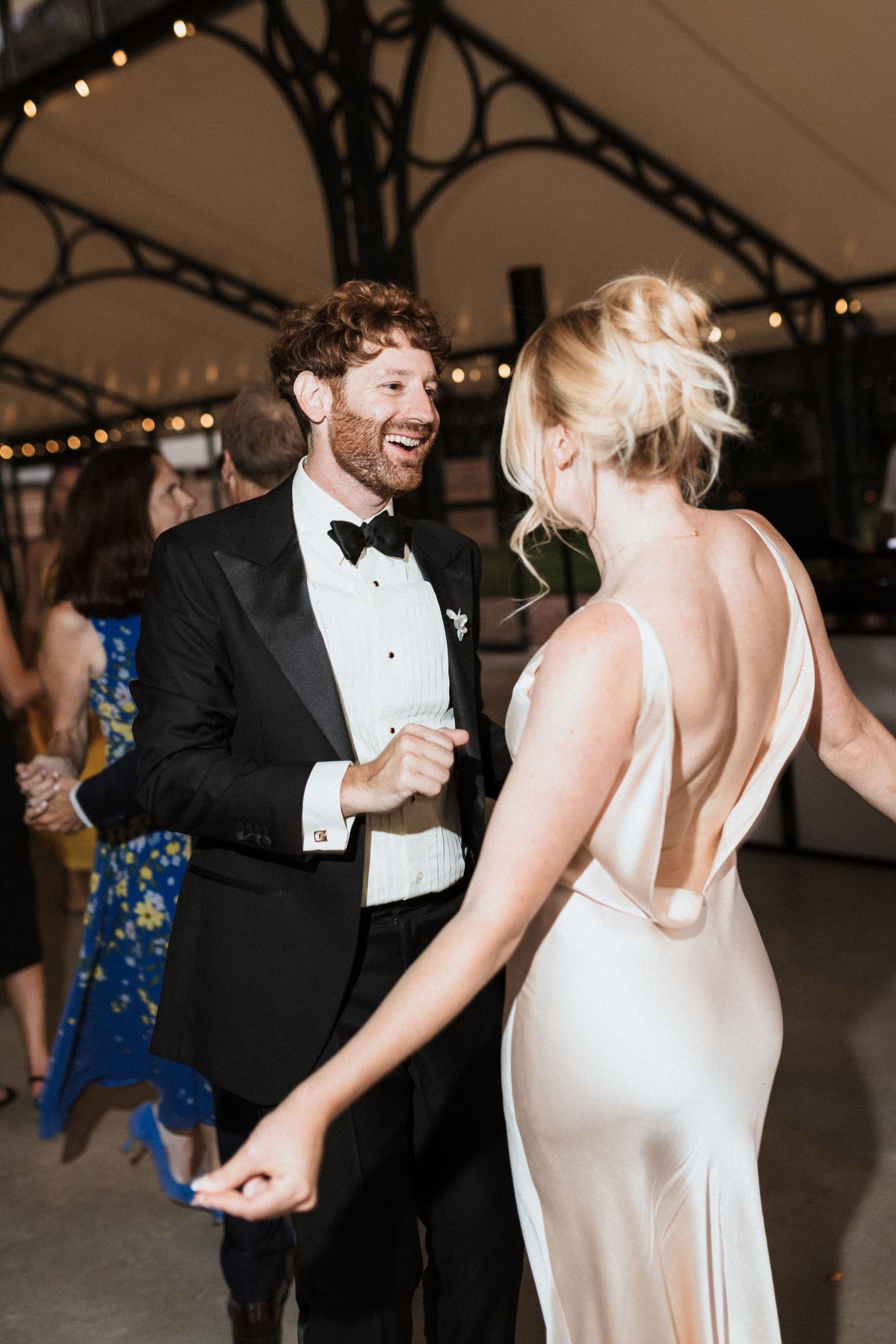 A couple shares a joyful dance moment at their wedding reception, with the bride in a sleek white gown and groom in classic tuxedo.