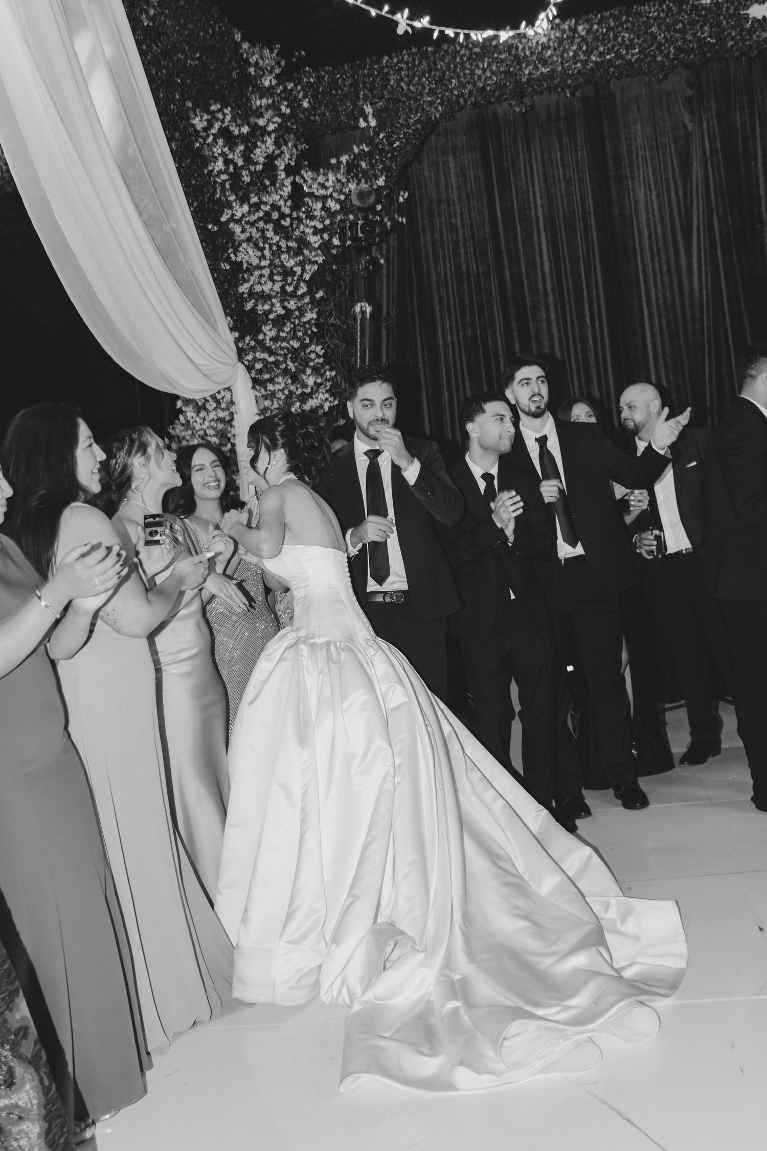 Black and white photo of bride and groom celebrating with wedding guests and groomsmen at elegant reception.
