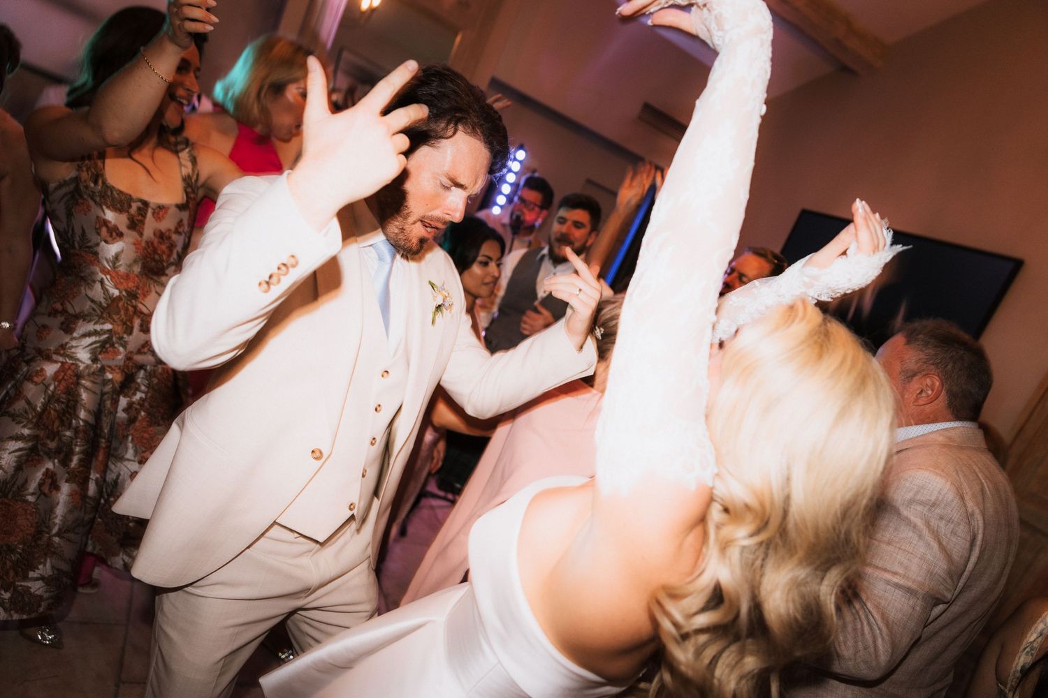 Wedding reception dance party with guests celebrating in dimly lit venue.