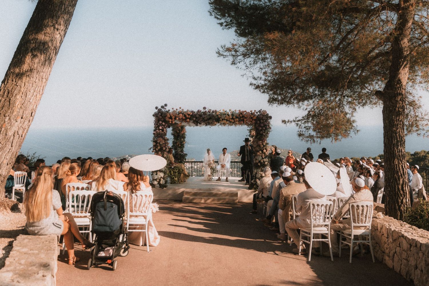 Elegant outdoor wedding reception setup with white chairs and tables overlooking a scenic coastal view.