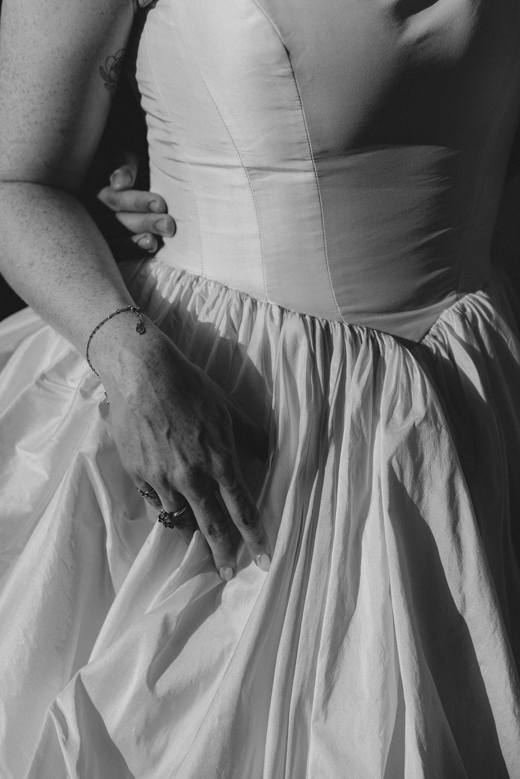 Close-up details of a white wedding dress showing the pleated skirt and bodice in a black and white photograph.