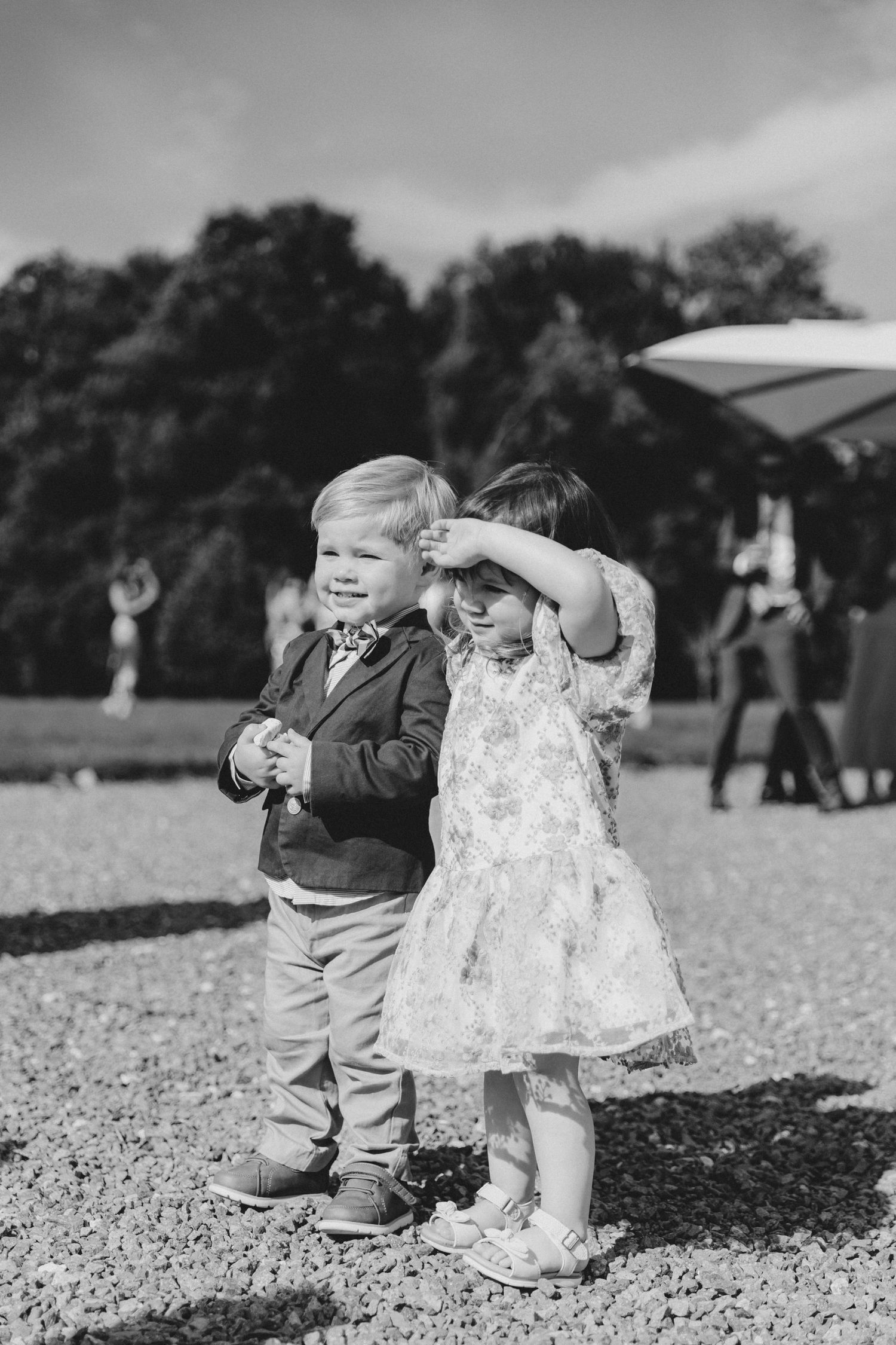 Two young children in formal attire stand together at an outdoor event.