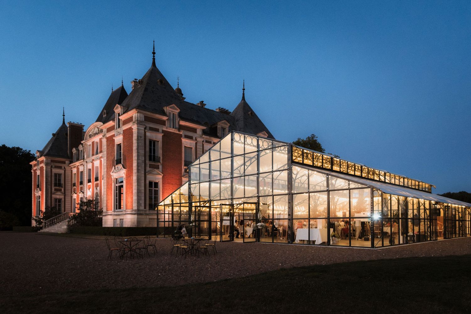Illuminated historic château with modern glass extension glowing at dusk against a deep blue evening sky.