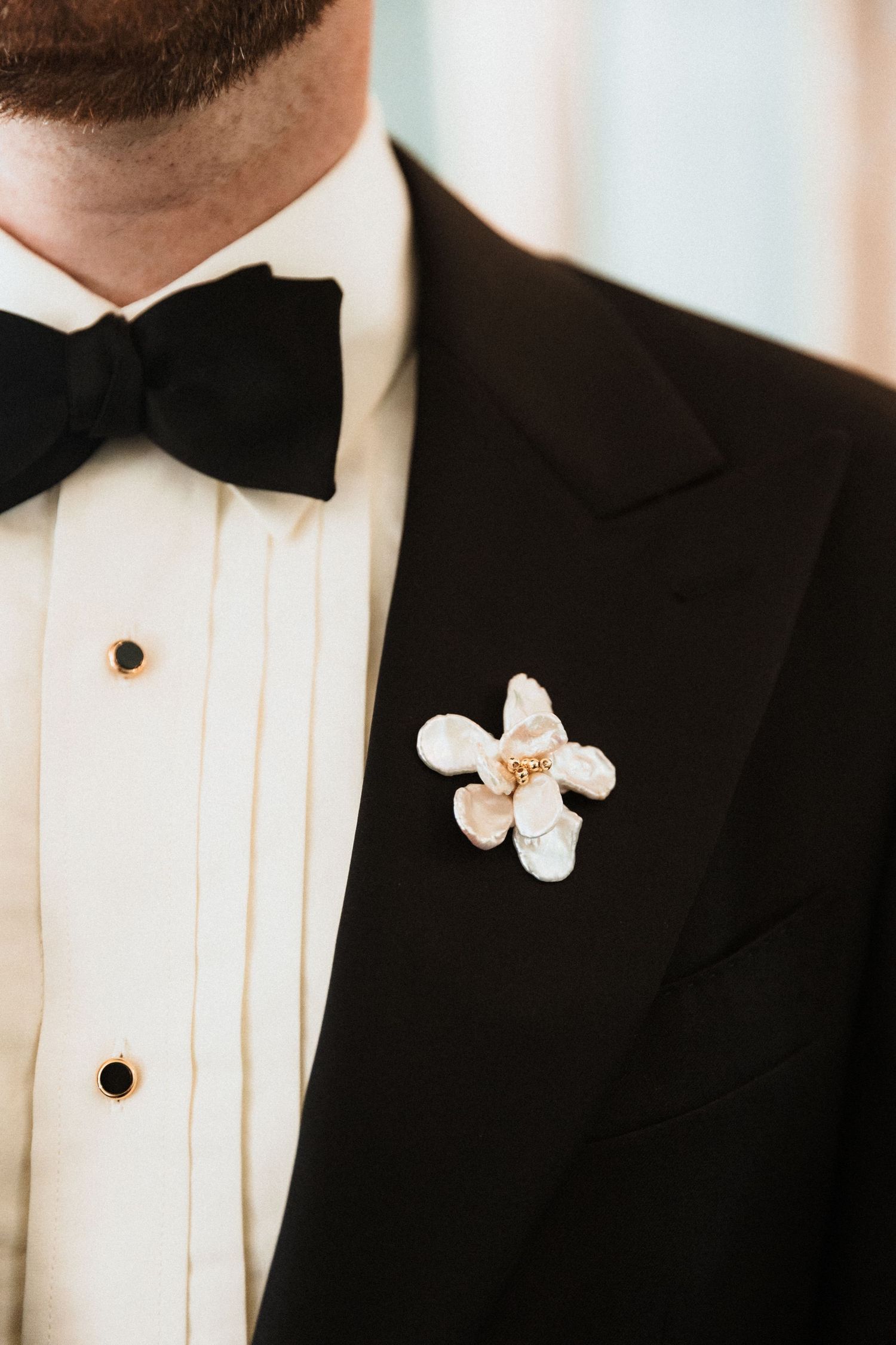 Man in black tuxedo with bow tie wearing a white floral boutonniere on his lapel.