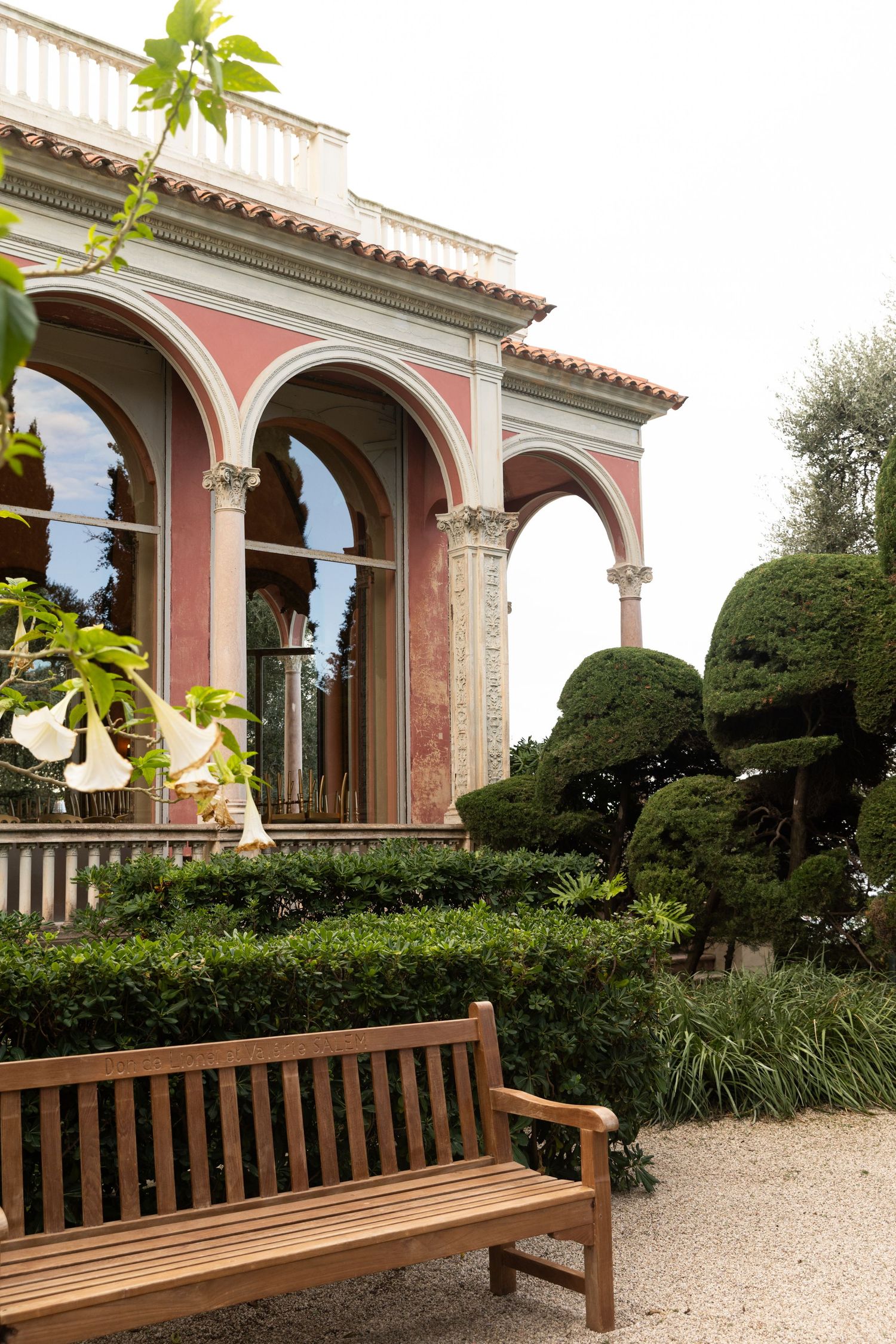 Villa Ephrussi de Rothschild - Wooden bench in front of a pink Italian villa with arched windows and manicured topiary garden.