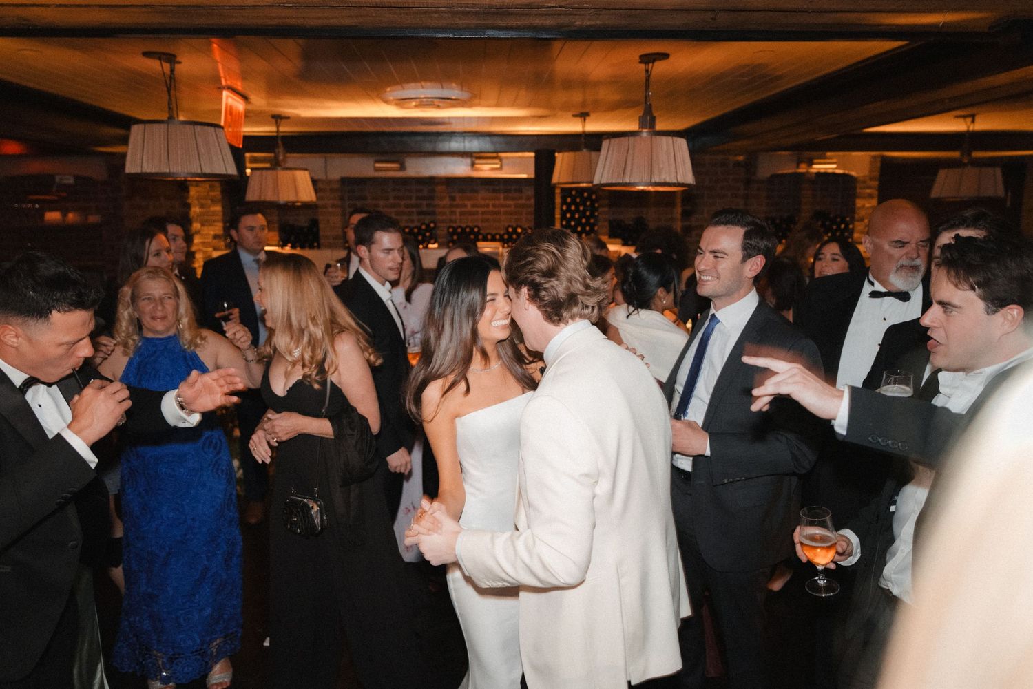 Elegant wedding reception with guests dancing in formal attire at a warmly lit venue.