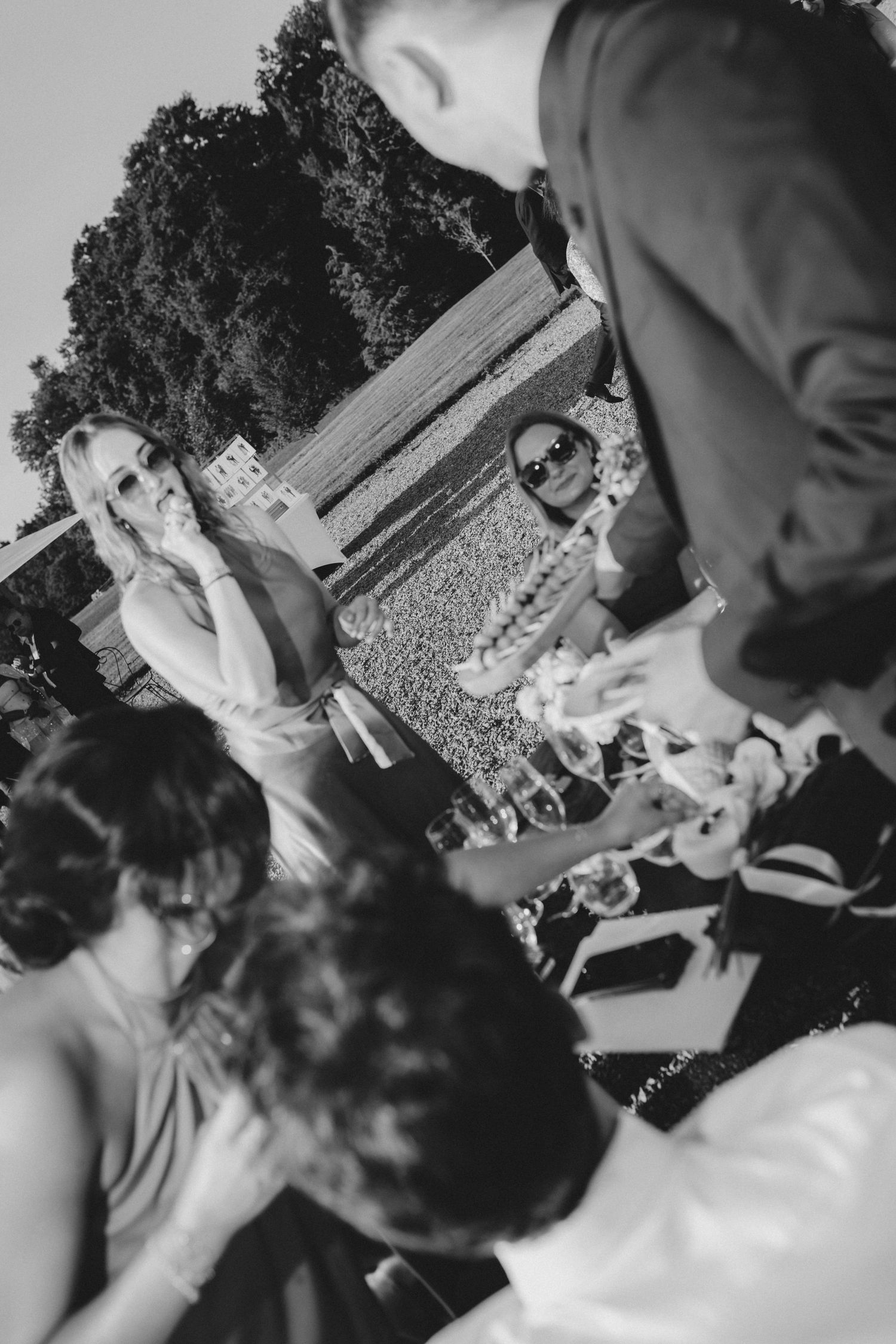 Black and white photo of wedding guests dancing and celebrating at an outdoor venue.