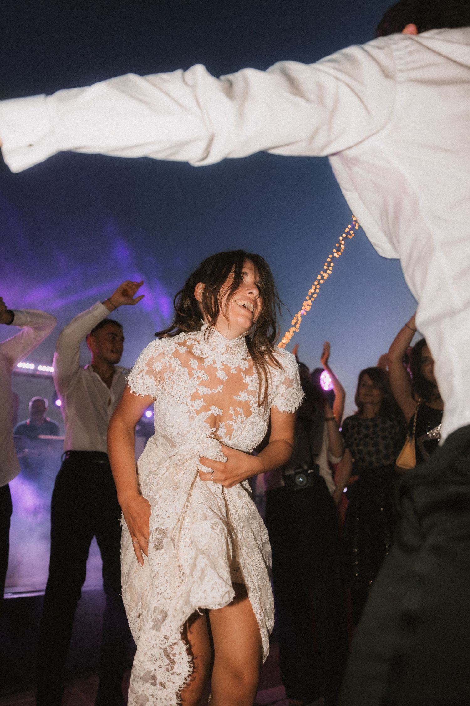 Wedding celebration on dance floor with guests dancing in evening lighting.