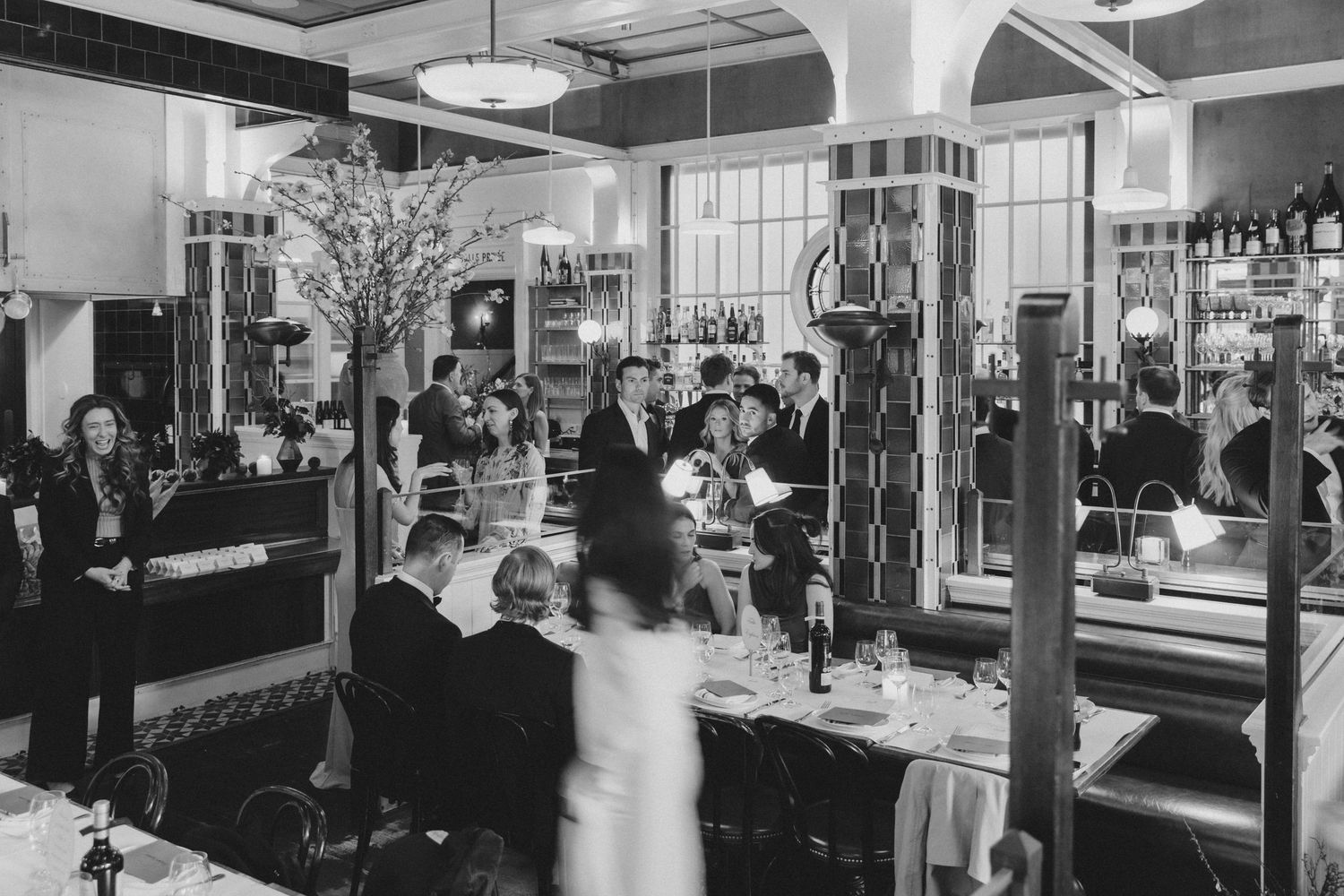 Black and white photo of an elegant, busy Art Deco restaurant with diners and staff in formal attire.