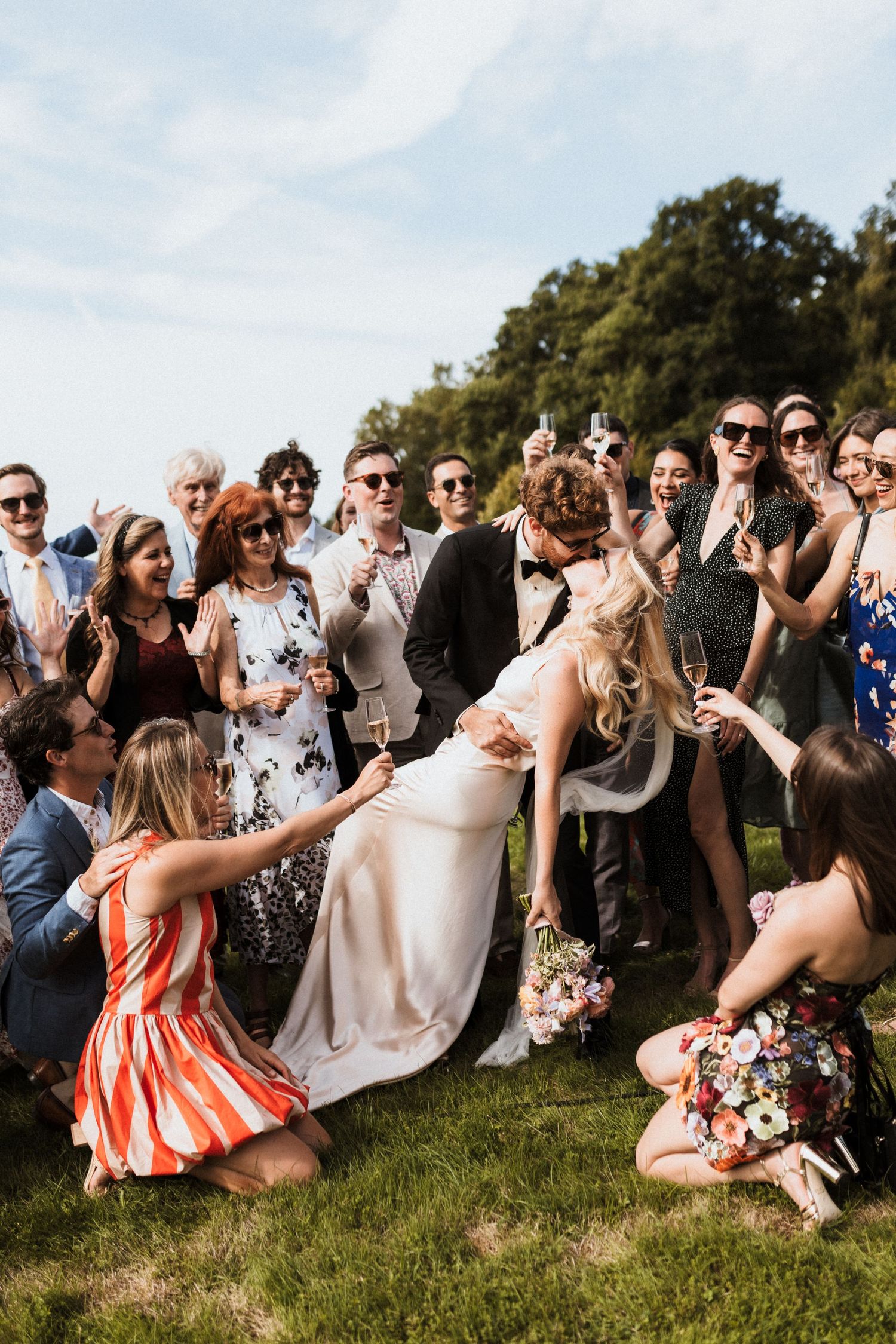 Wedding guests gather on a grassy hillside to watch and celebrate during an outdoor ceremony.