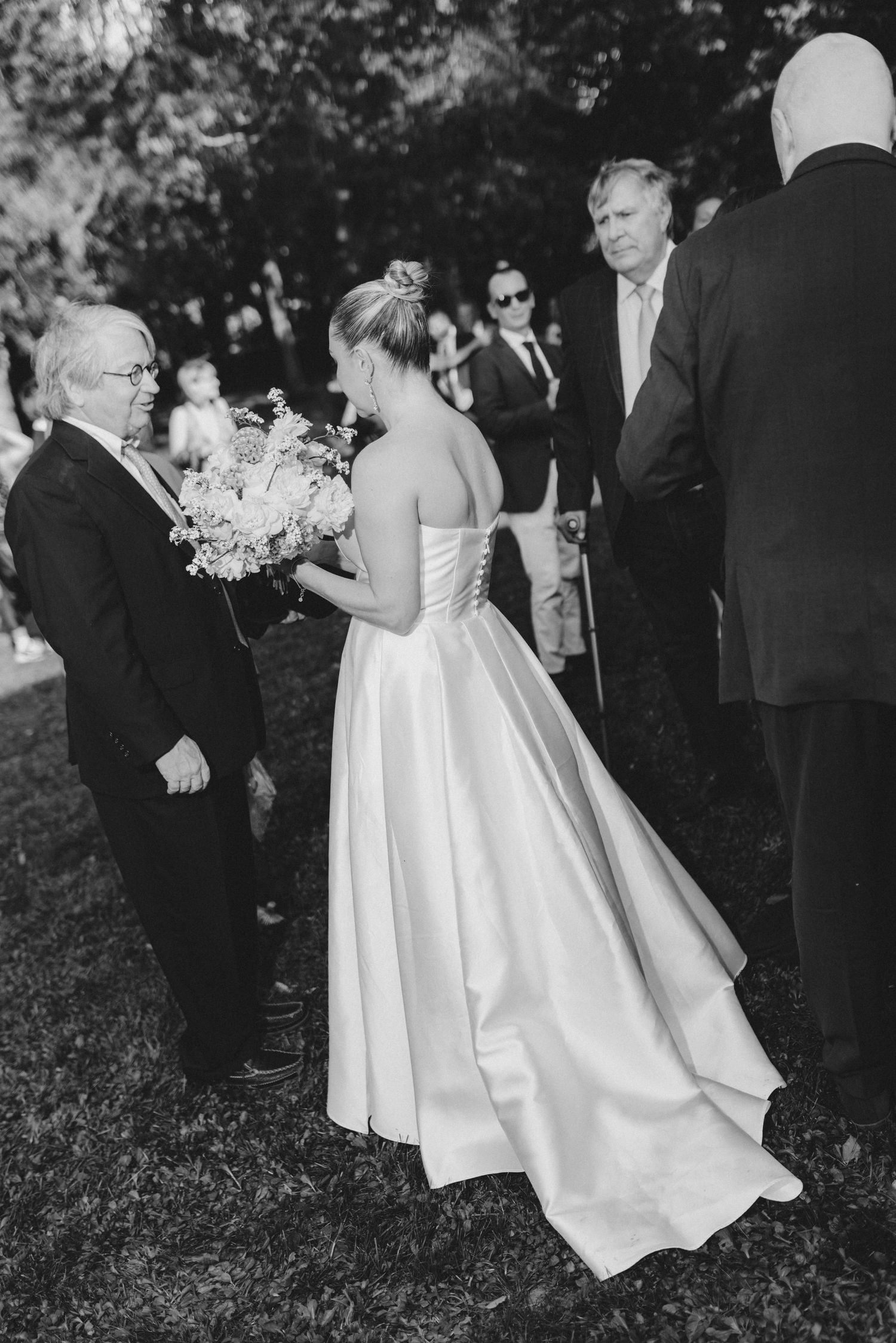 Black and white photos show a bride in a flowing white dress walking through a garden setting during a wedding ceremony.