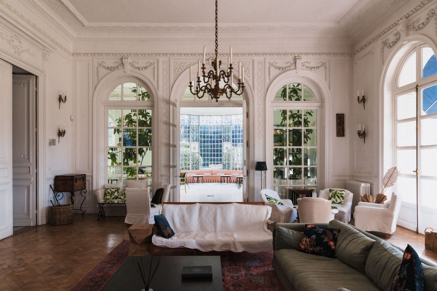 Villa Rocabella Elegant -French-style living room with arched windows, ornate moldings, chandelier, & classic furnishings on hardwood floors