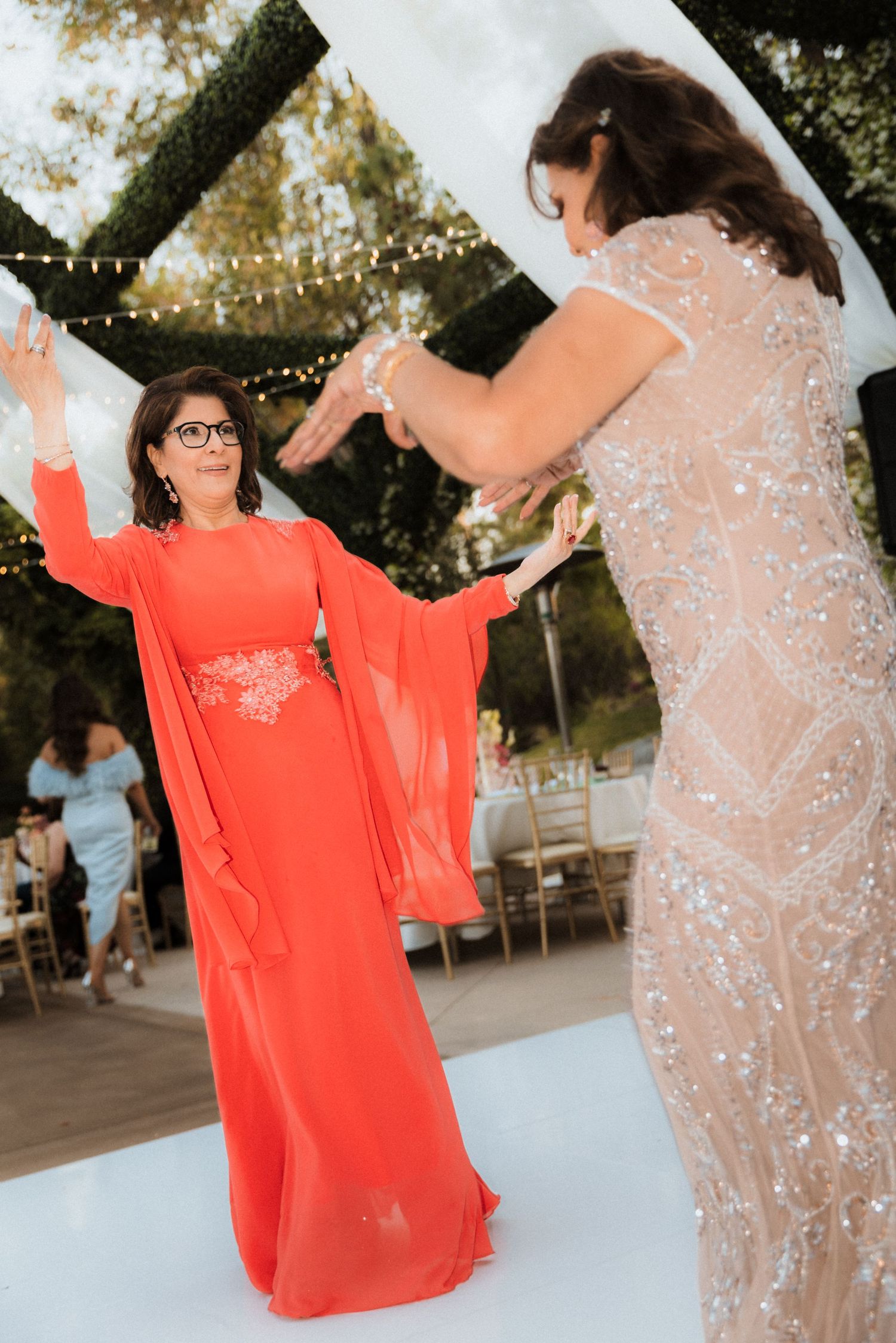 People dancing and celebrating at an outdoor party with string lights and trees in the background.