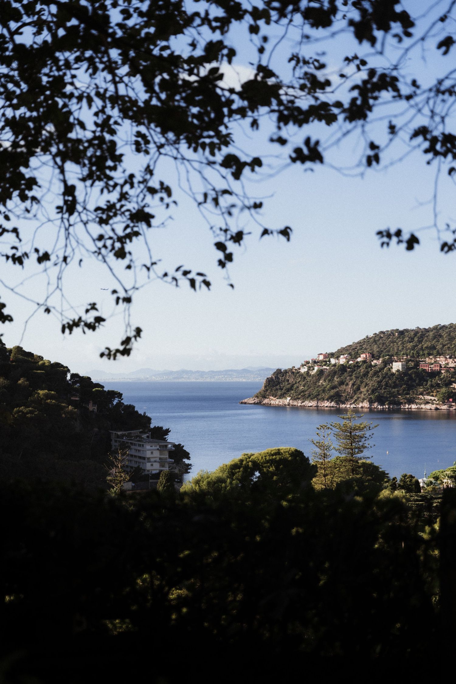 Panoramic coastal view of a Mediterranean hillside town nestled between blue sea and lush vegetation under bright sky.