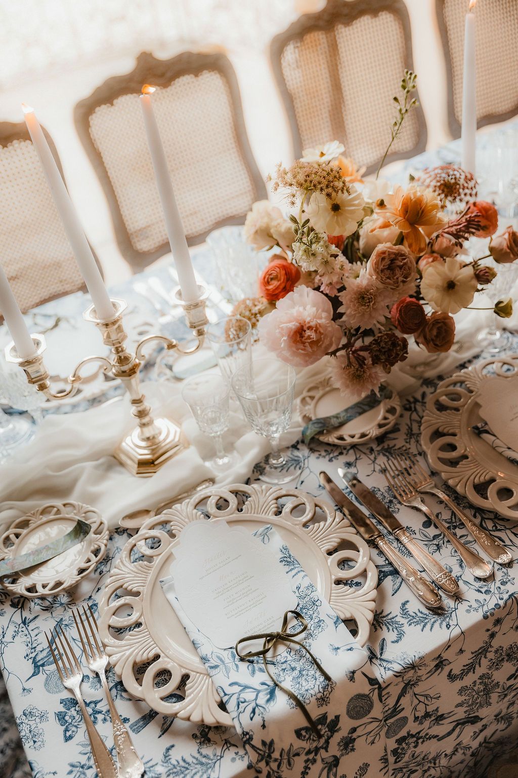 Elegant table setting with peach and cream floral centerpieces and ornate patterned linens.